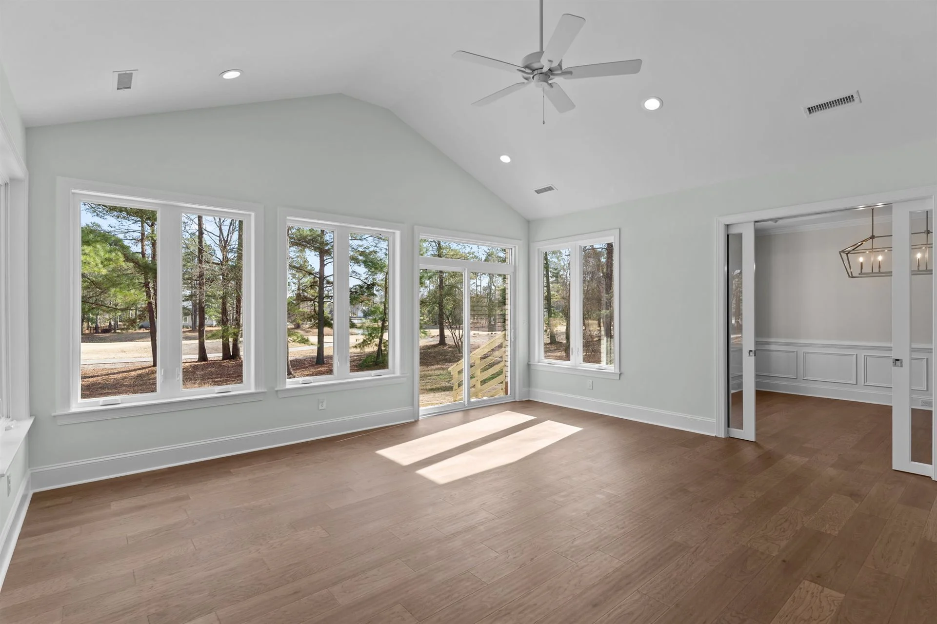Spacious room with large windows, glass doors, hardwood floors, ceiling fan, and adjoining dining area. Ideal design by a modern home builder.