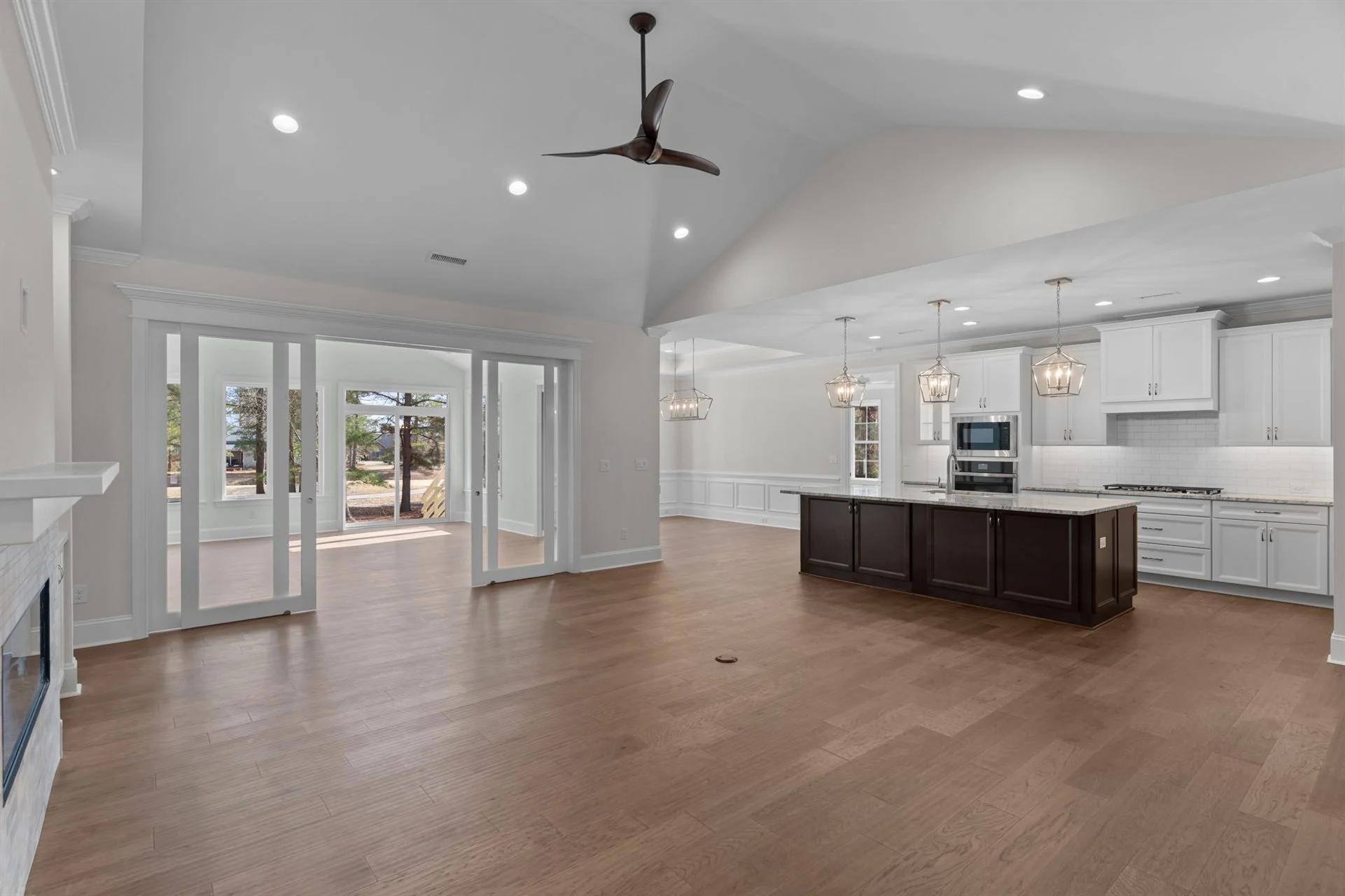 Spacious open-concept kitchen and living area with wooden floors, elegant lighting, and large sliding doors, showcasing home builder craftsmanship.