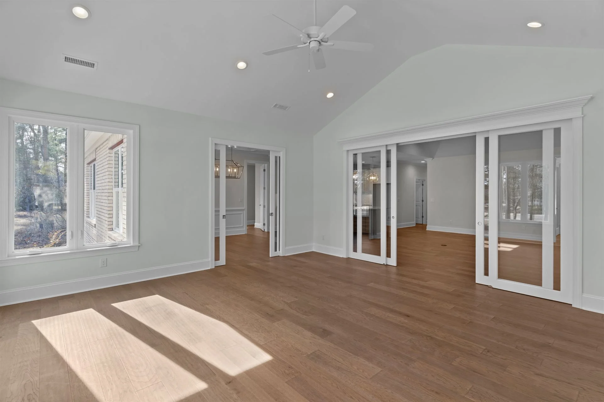Spacious living area with hardwood flooring, large windows, glass sliding doors, and white walls; ideal for home builder inspiration.