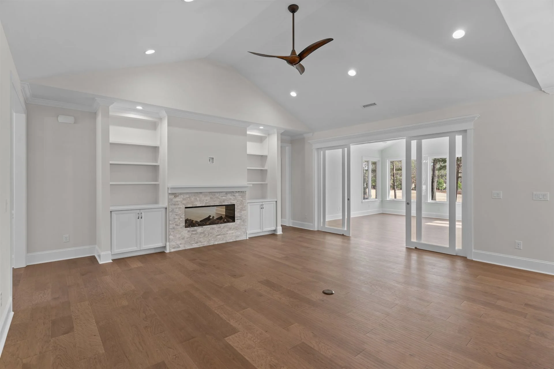 Spacious living room with wood floors, modern ceiling fan, built-in shelves, fireplace, and sliding glass doors by a home builder.