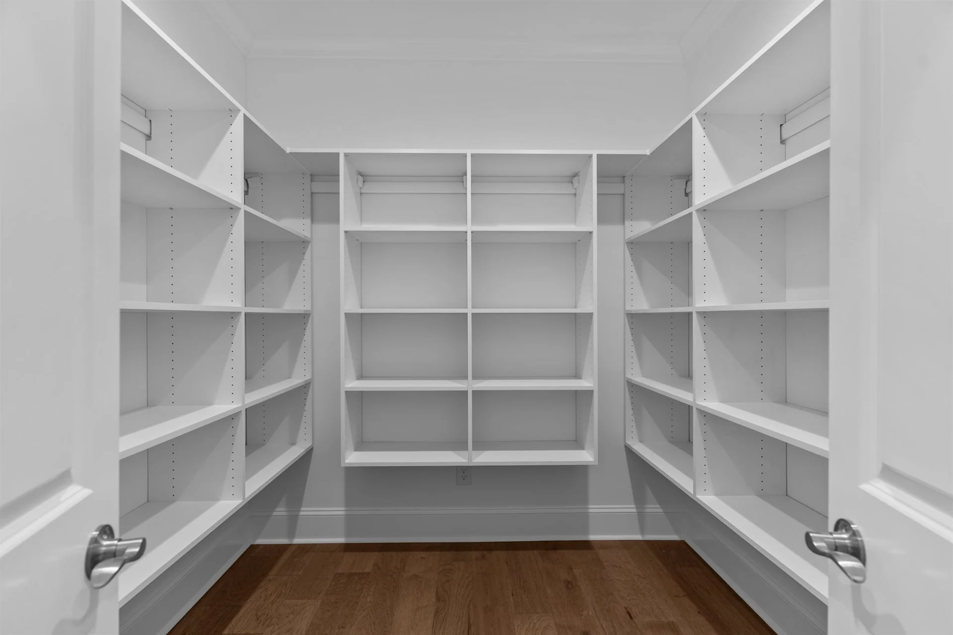 Spacious white pantry with built-in shelves on three walls, showcasing efficient storage design by a home builder. Wood floor adds warmth.