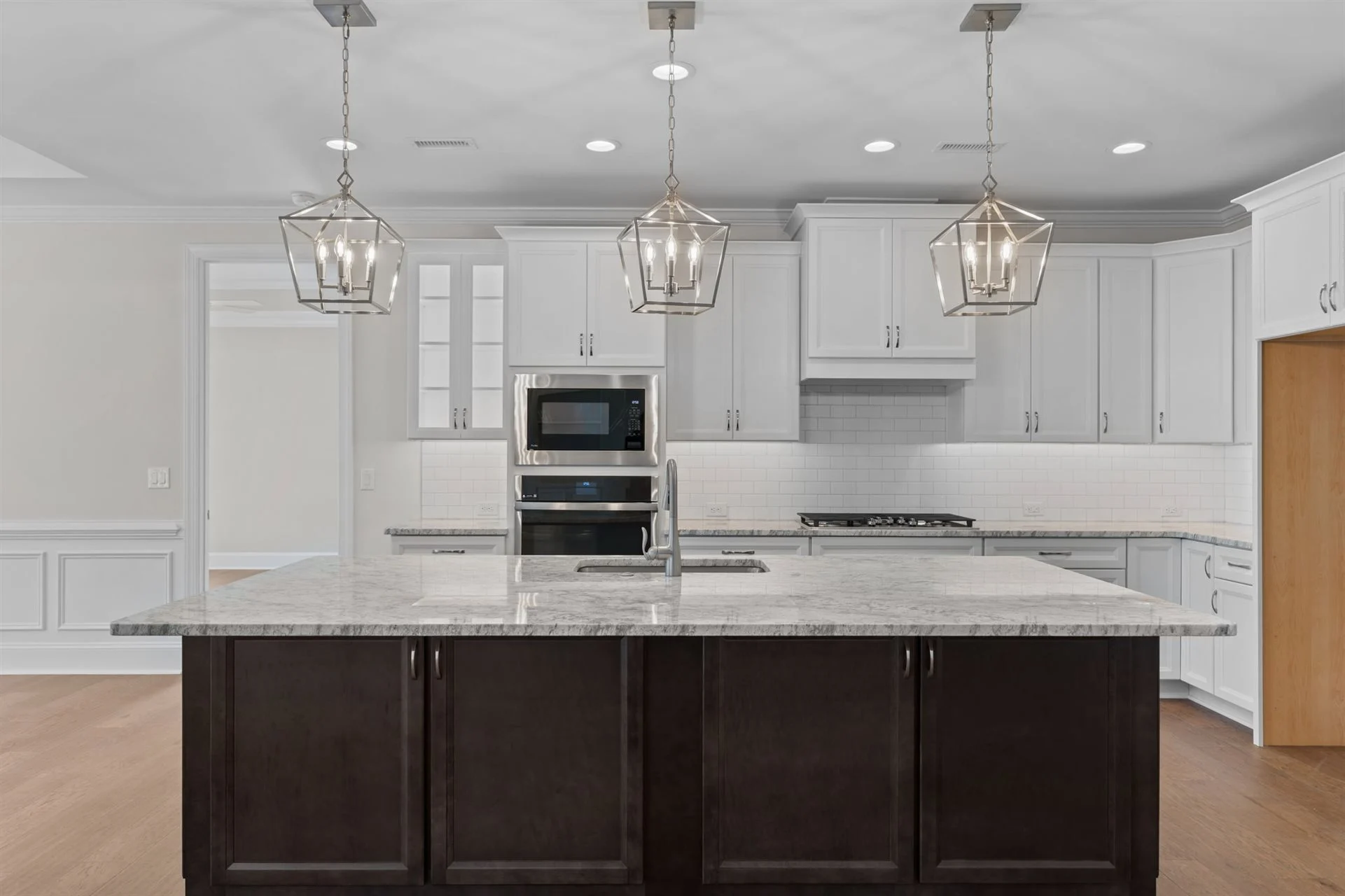 Modern kitchen with dark island, marble countertop, stainless appliances, and stylish pendant lights, showcasing home builder craftsmanship.