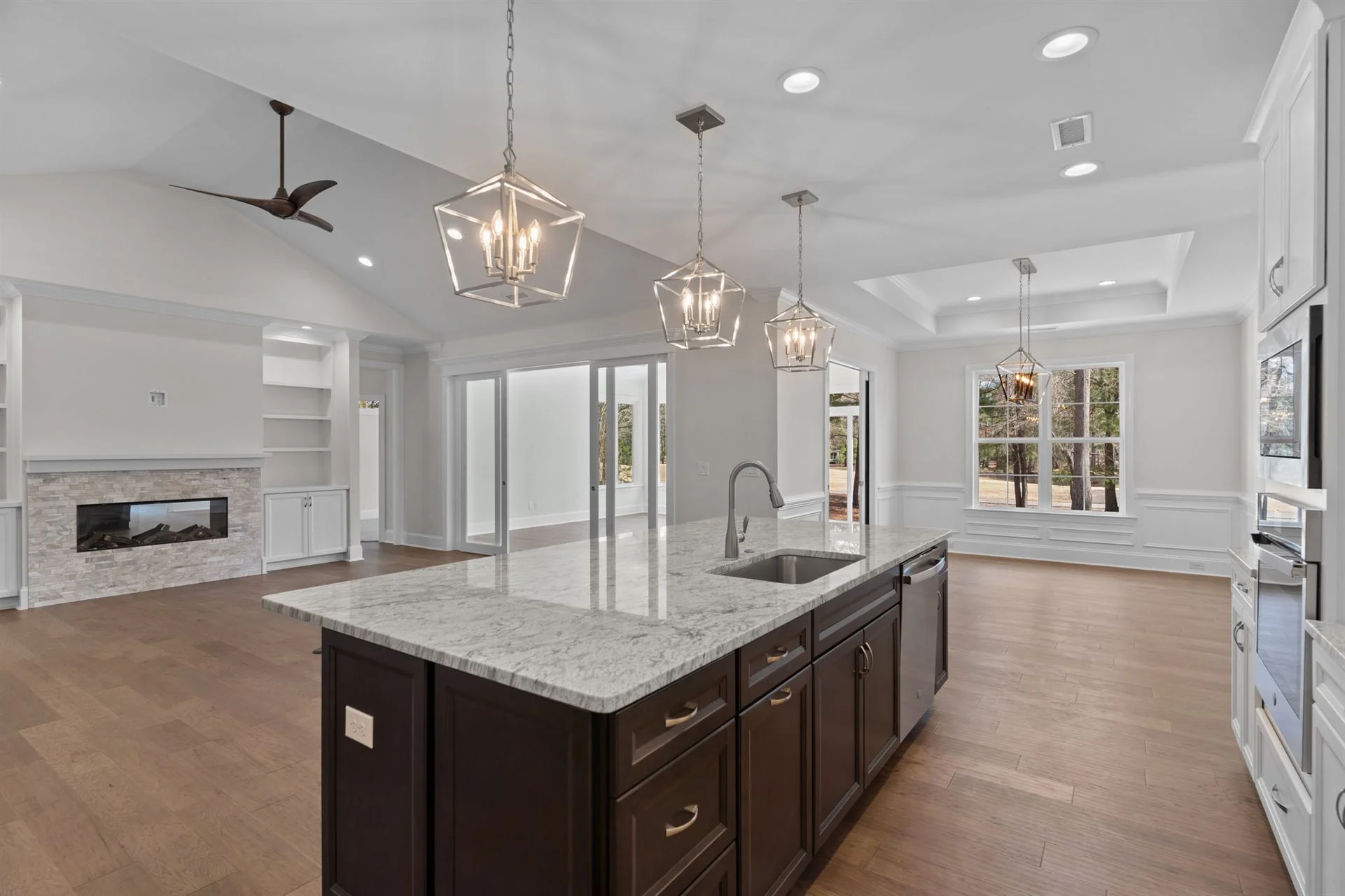 Spacious open-concept kitchen and living area by home builder, featuring granite island, pendant lights, fireplace, and large windows.