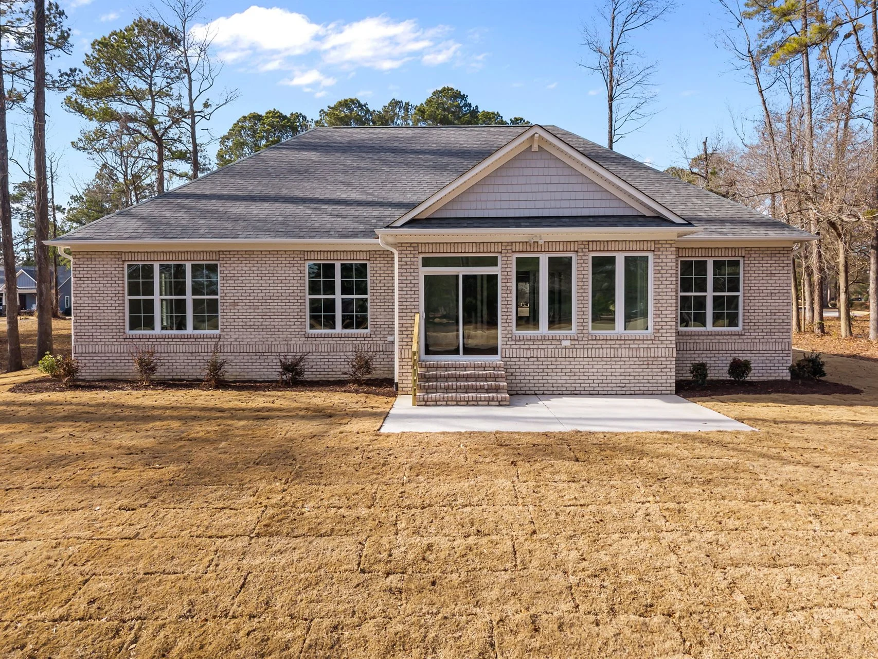 Single-story brick house with large windows and a manicured lawn, surrounded by trees, showcasing new home builder craftsmanship.
