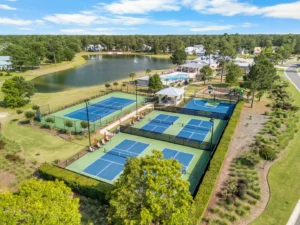 Tennis and basketball courts next to a lake and swimming pool, surrounded by greenery and new homes. Ideal setting for a home builder community.