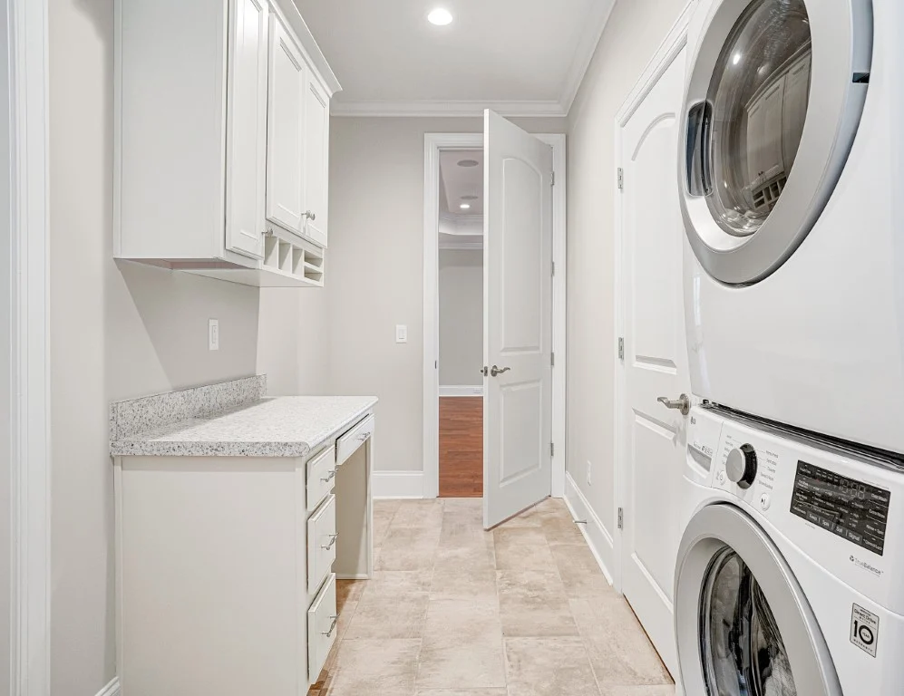 Laundry room with stacked washer, dryer, white cabinets, and a granite countertop. Designed by a home builder.