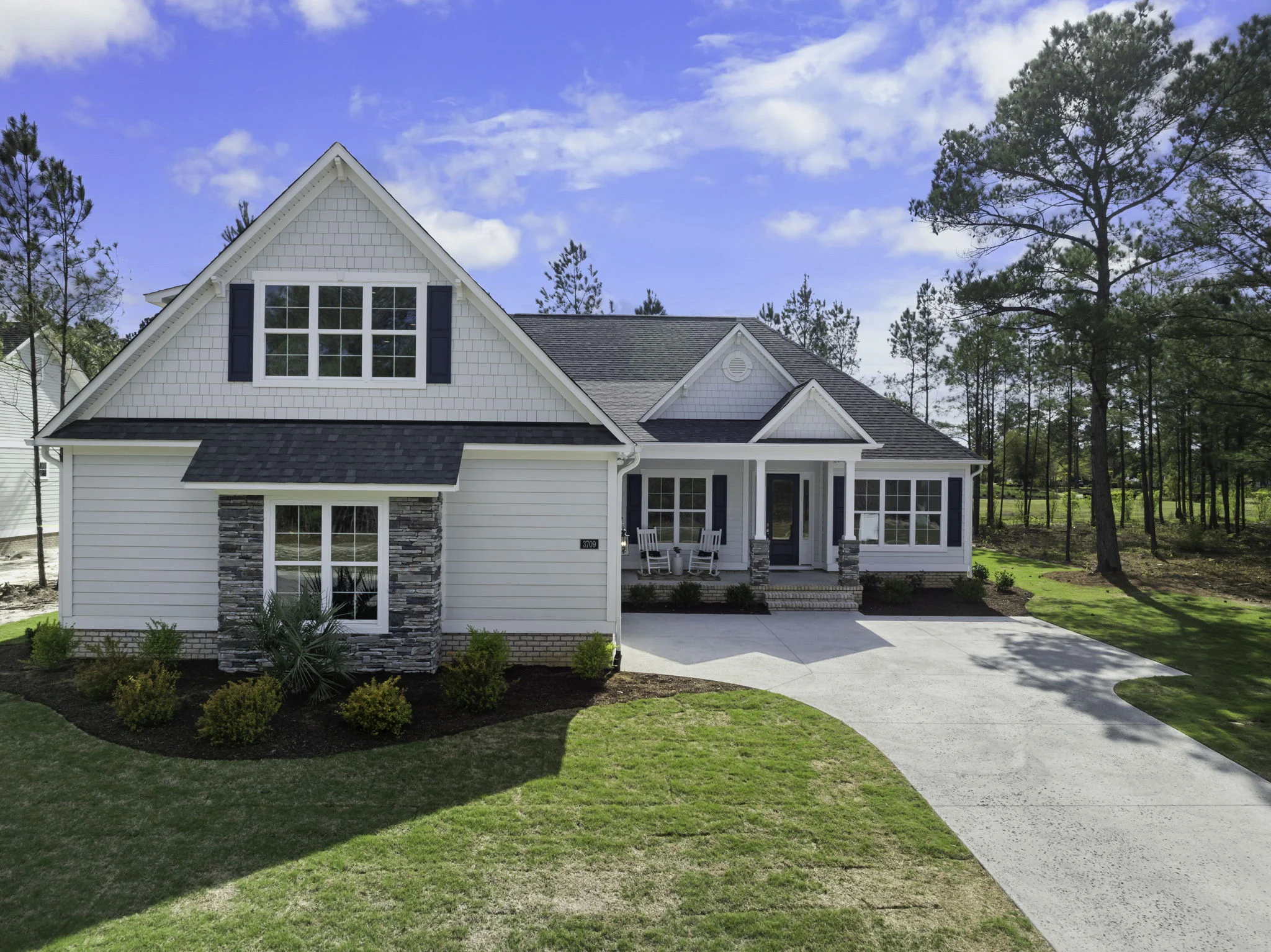 gallery-exteriors (20) Modern, single-story house with brick and stone accents, surrounded by trees. Ideal for a home builder looking for serene settings.