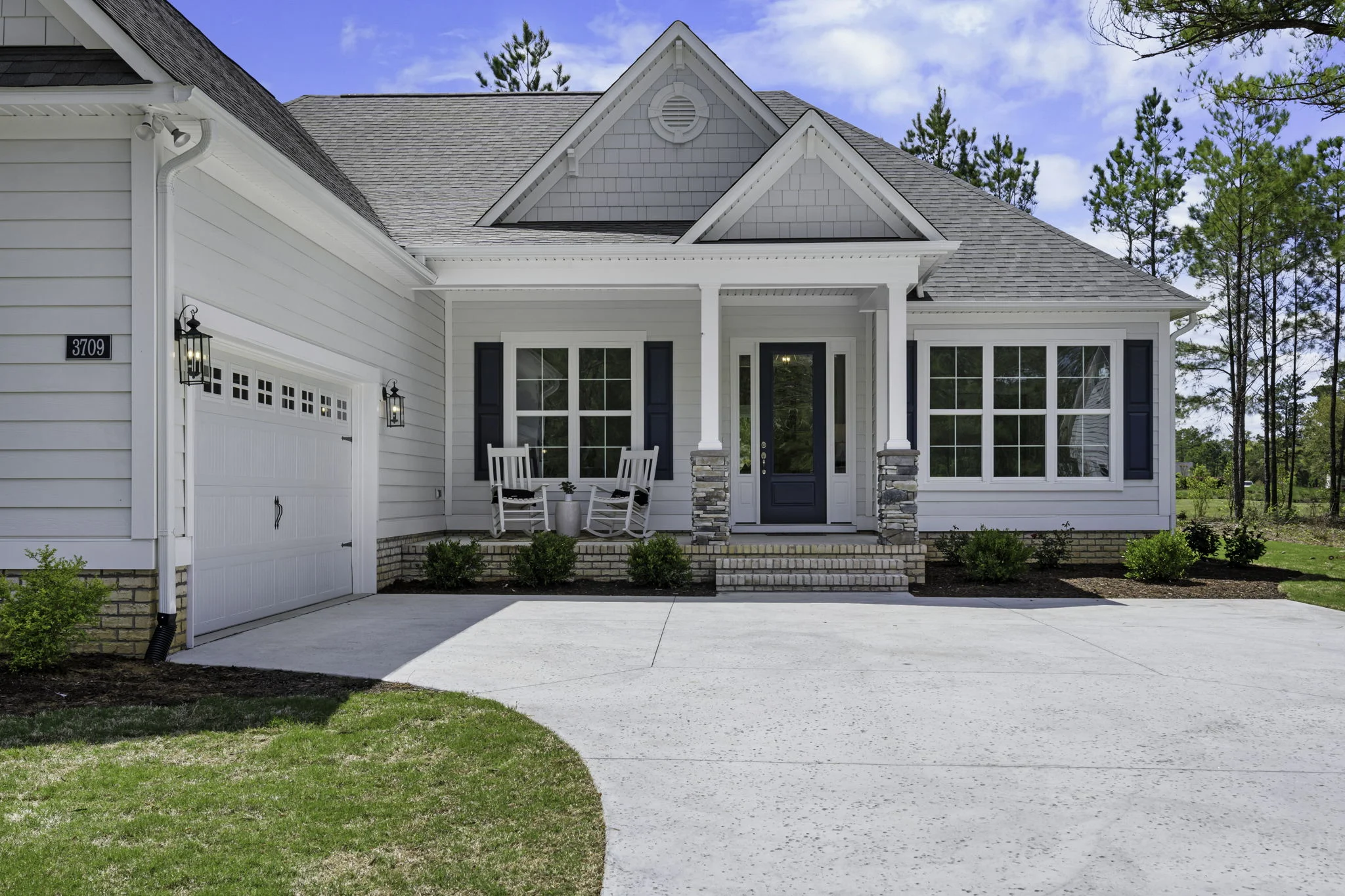 gallery-exteriors (21) Modern single-story home with gabled roof, white siding, two rocking chairs on porch; exemplary work of a home builder.