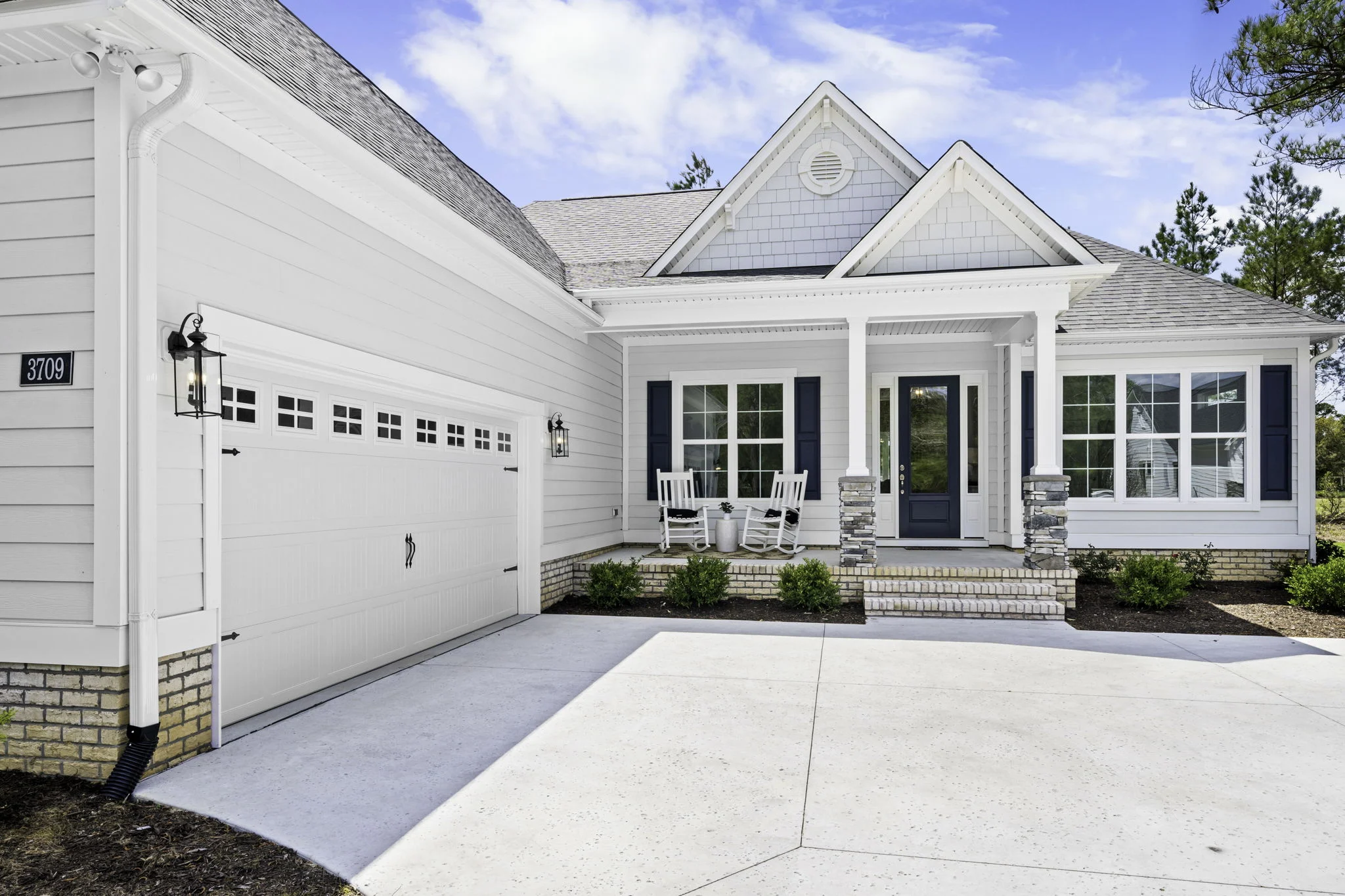 gallery-exteriors (22) Modern white house with a spacious garage, inviting front porch, rocking chairs, and neatly landscaped yard. Ideal design by a home builder.