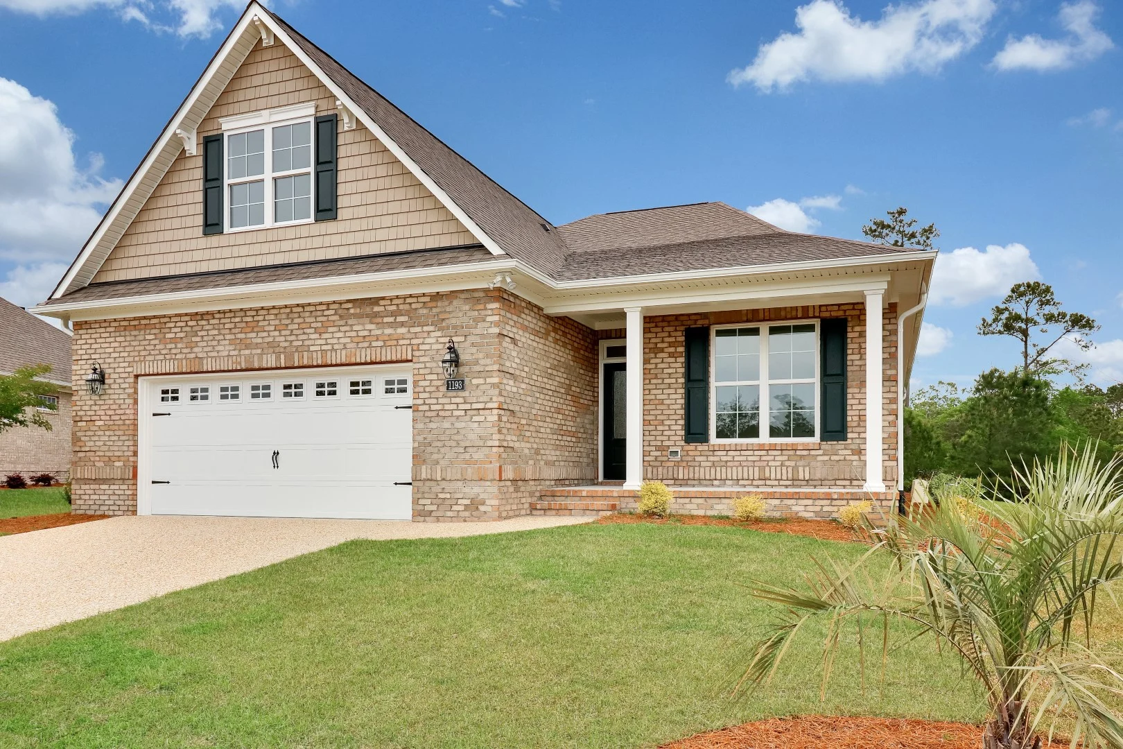 gallery-exteriors (27) Brick house with gabled roof, double garage, manicured lawn, and shrubs. Ideal for home builders showcasing design and curb appeal.