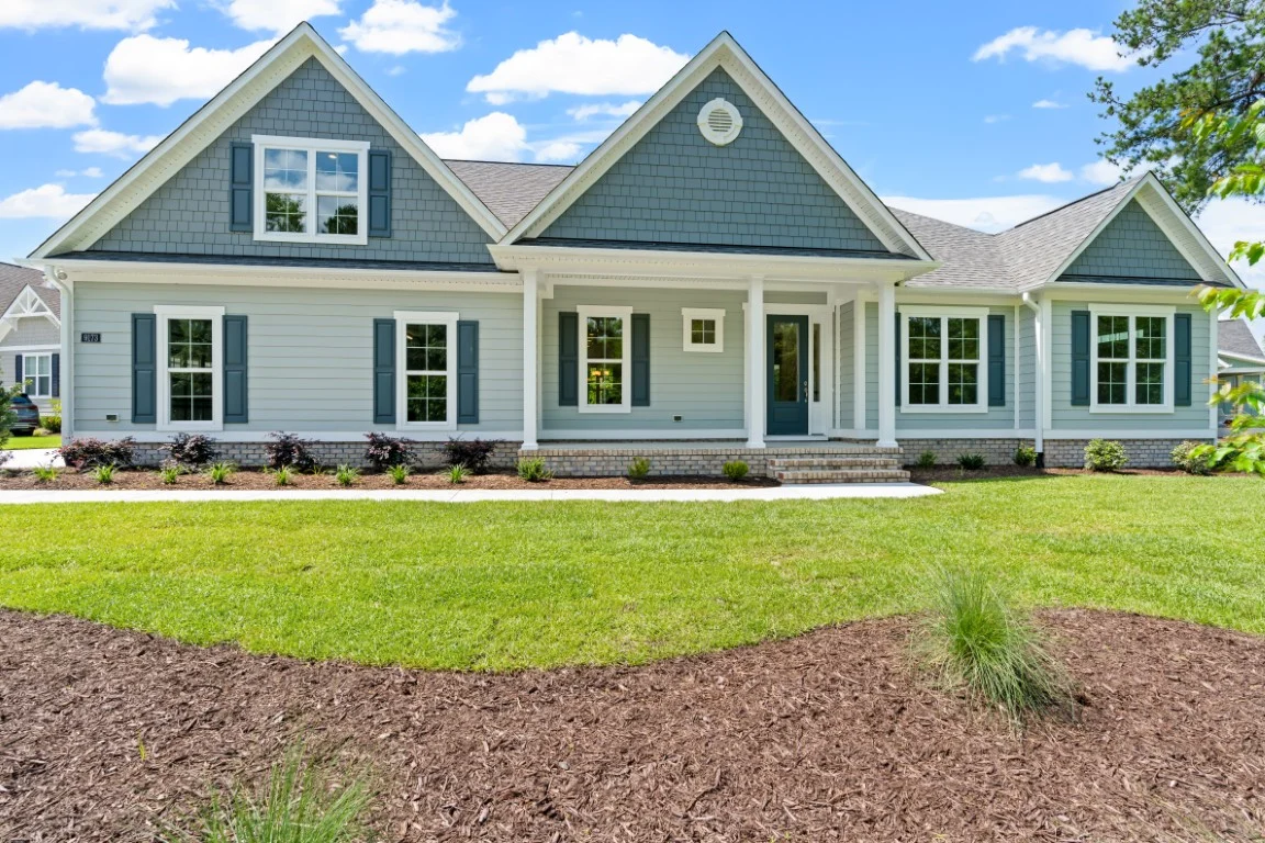 gallery-exteriors (30) Modern grey house with gabled roof and shutters, surrounded by landscaped yard. Ideal for home builder inspiration.