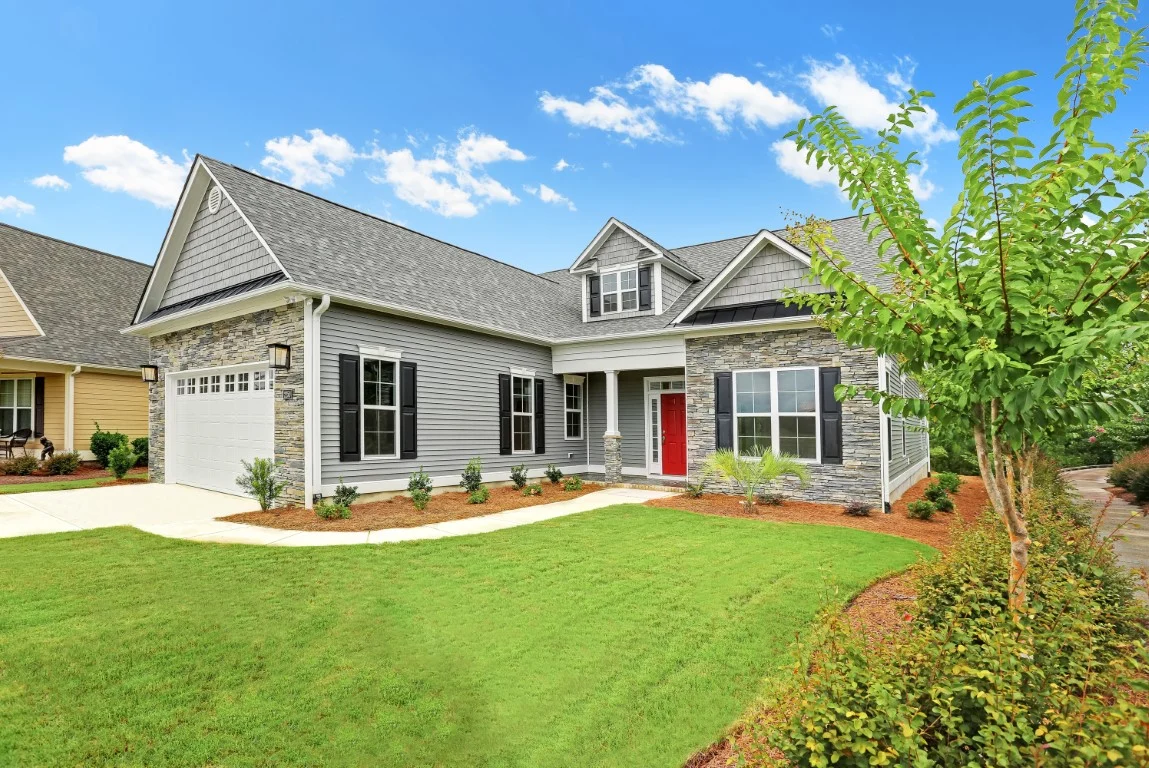 gallery-exteriors (35) Modern home with vinyl siding, stone facade, red door, manicured lawn, and garage. Showcasing quality craftsmanship by a home builder.