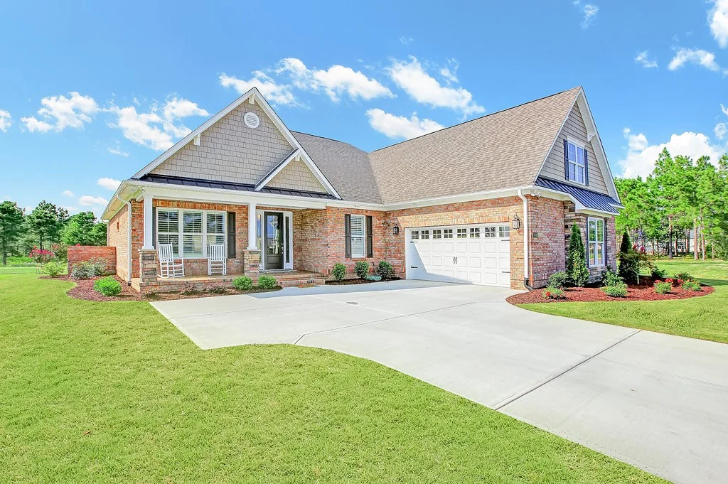 gallery-exteriors (7) Brick house with gable roof, landscaped yard, and attached garage. Represents the work of a meticulous home builder.