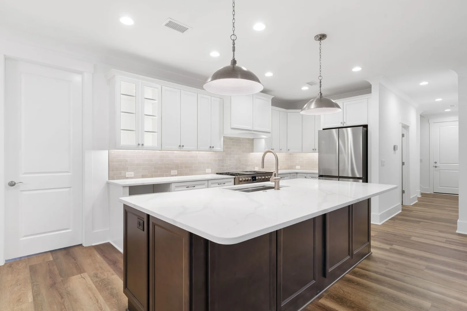 gallery-kitchen (11) Modern kitchen with spacious island, marble countertops, stainless steel appliances, and pendant lights. Sleek design by a home builder.