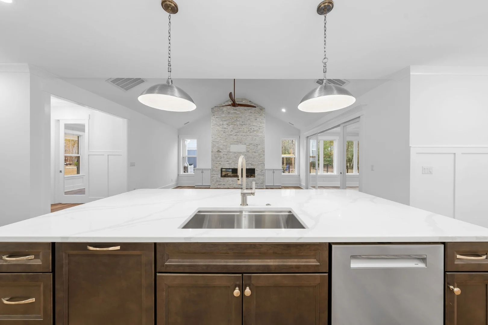 gallery-kitchen (18) Modern kitchen with white marble island, stainless steel sink, pendant lights, and view of living room with large windows, designed by a home builder.