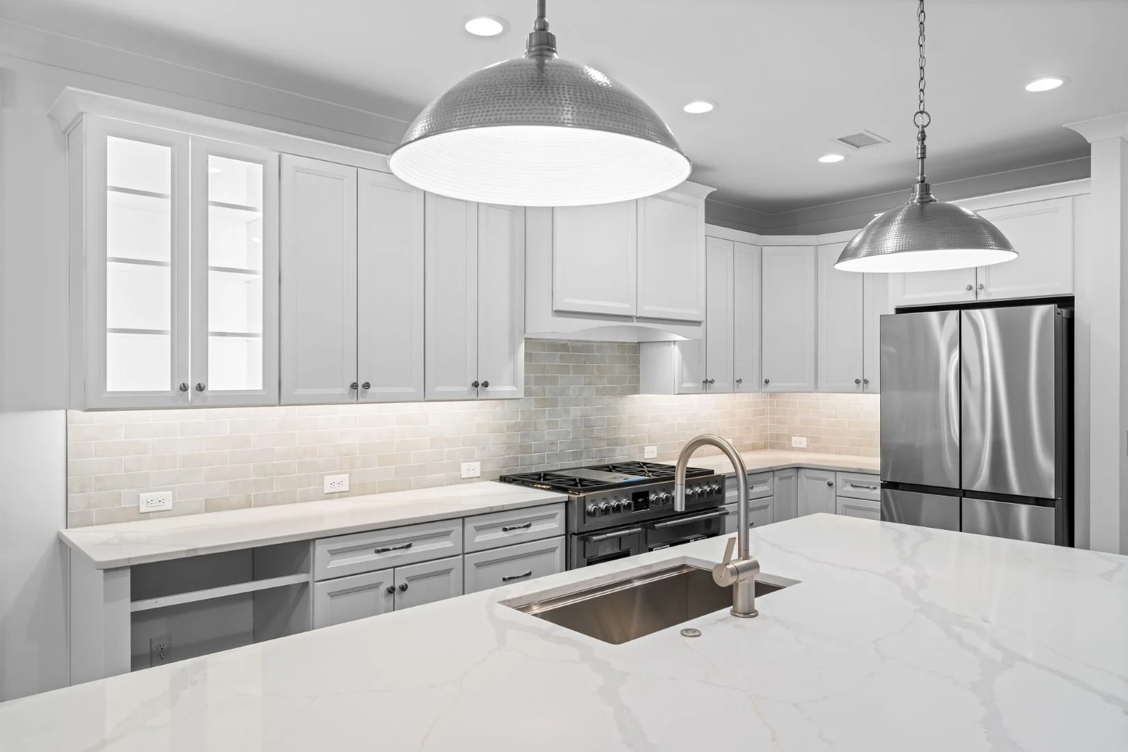 gallery-kitchen (19) Modern kitchen with white cabinetry, stainless steel appliances, large island, and pendant lights. Designed by a professional home builder.
