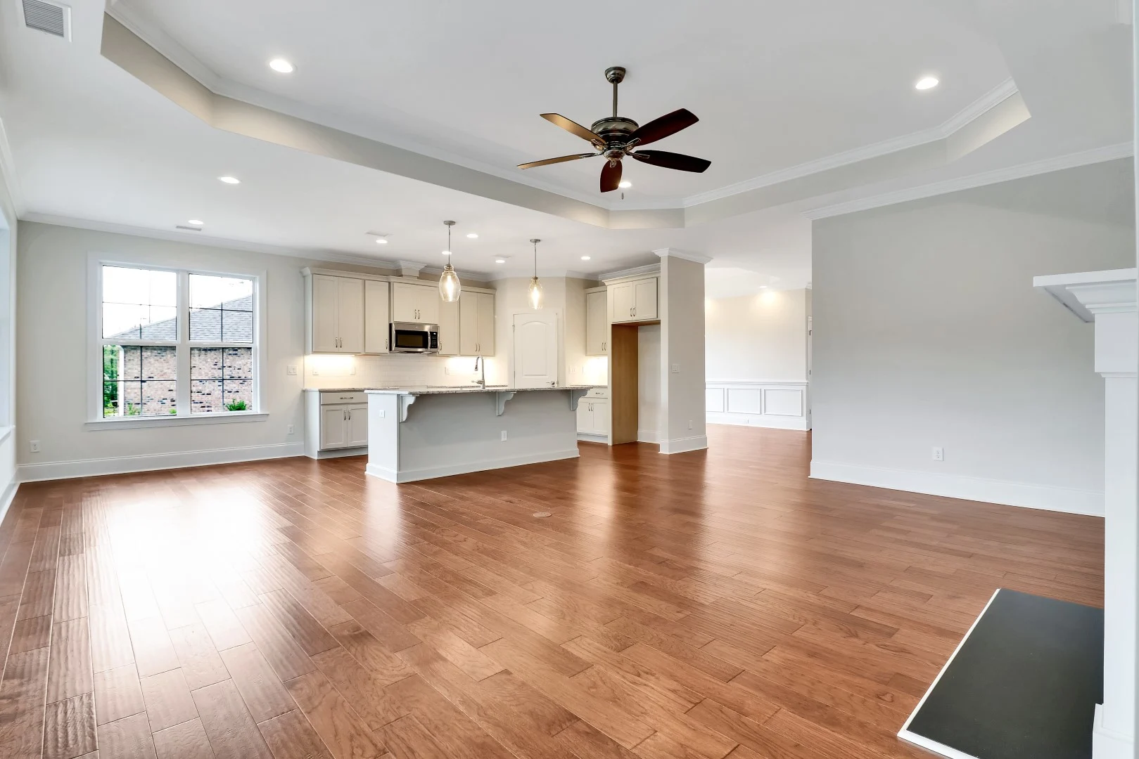 gallery-kitchen (26) Spacious modern living area with wooden floors, ceiling fan, and open kitchen. A home builder's craftsmanship is evident in the detail.
