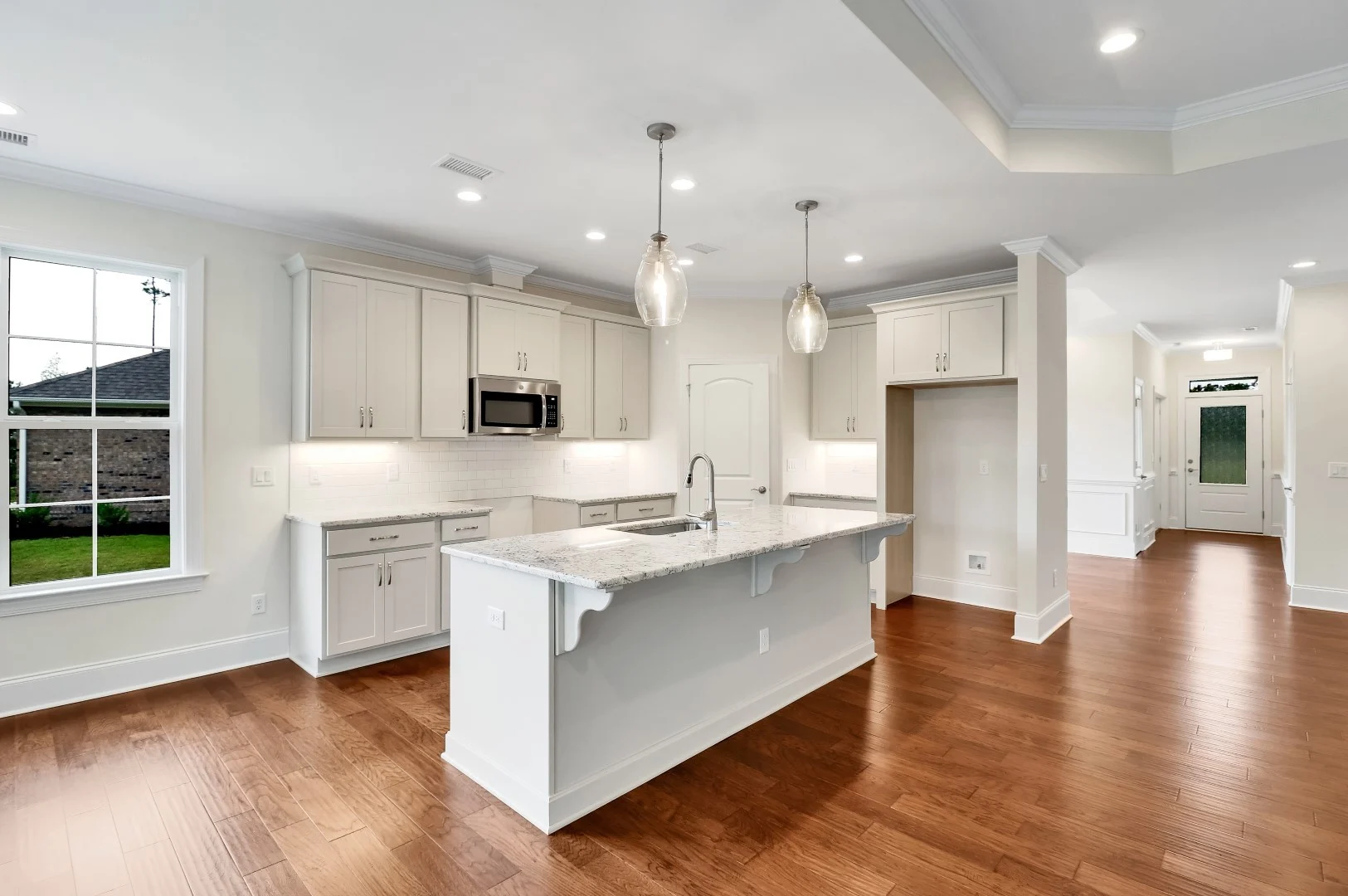 gallery-kitchen (28) Modern kitchen by home builder, featuring white cabinetry, granite countertops, island, pendant lighting, stainless appliances, and hardwood floors.