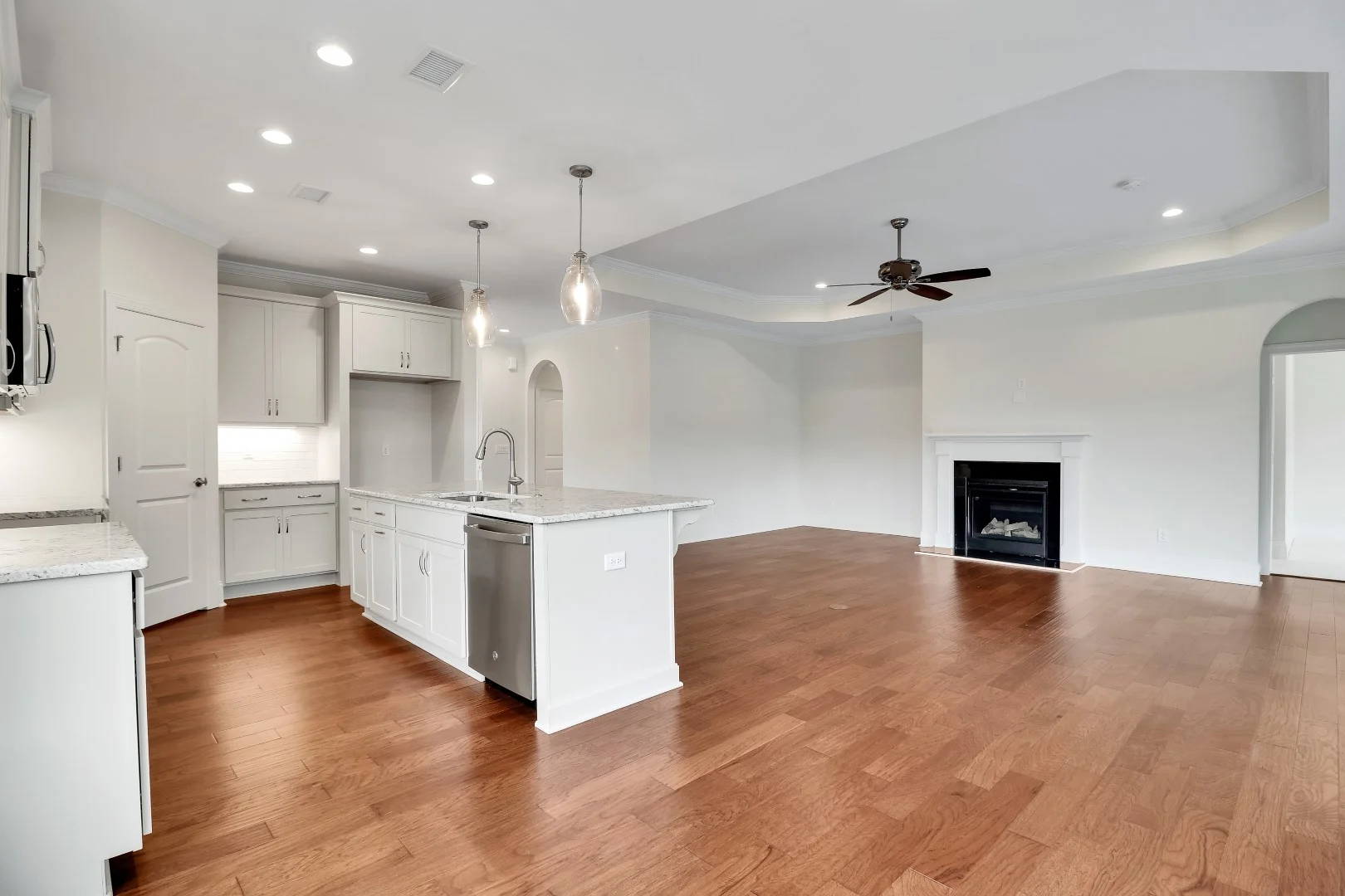 gallery-kitchen (29) Spacious open-concept kitchen and living room with hardwood floors, white cabinetry, island, pendant lights, and fireplace. Ideal for home builder ins