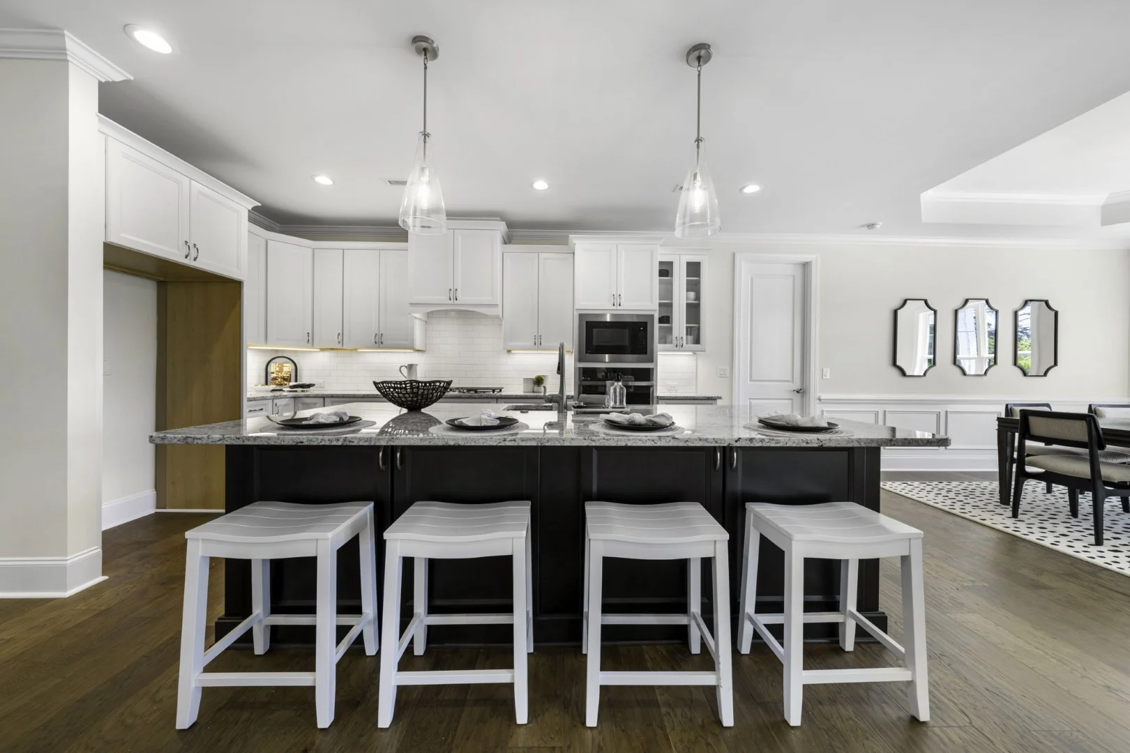 gallery-kitchen (3) Spacious kitchen with white cabinets, island bar seating, pendant lights, and dining area, exemplifying modern home builder design.