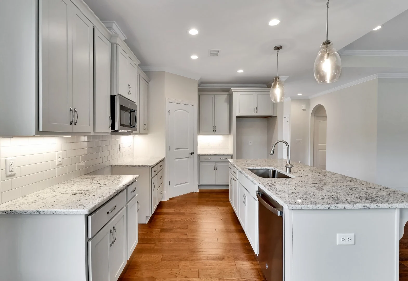 gallery-kitchen (31) Modern kitchen with granite countertops, stainless steel appliances, white cabinets, and pendant lighting. Ideal for home builder showcases.