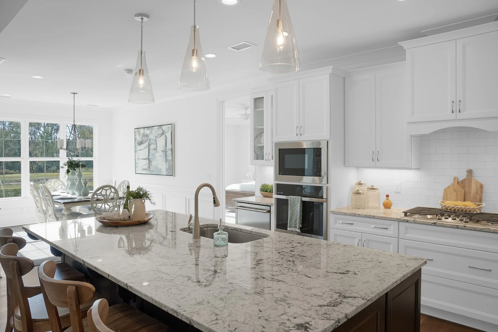 gallery-kitchen (33) Modern kitchen with marble island, wooden chairs, white cabinetry, modern appliances, and adjacent dining area. Spacious design by home builder.