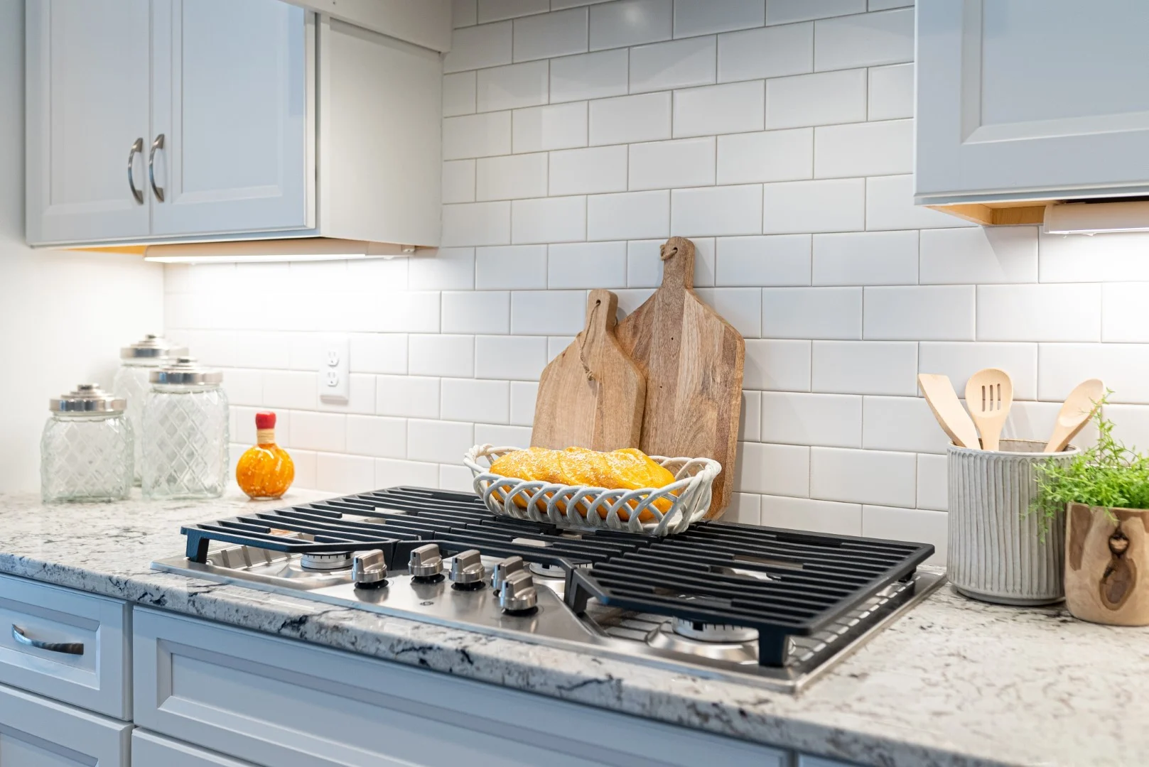 gallery-kitchen (34) Modern kitchen by home builder with marble countertop, gas stove, cutting boards, and basket of lemons against white subway tile backsplash.