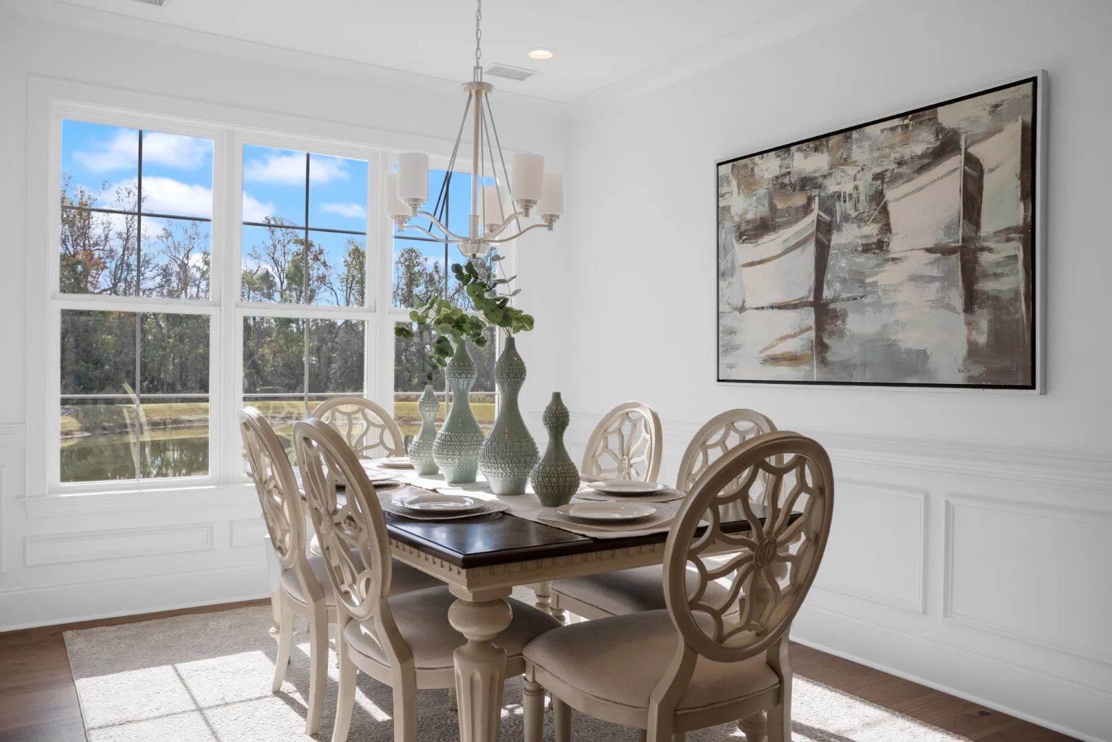 gallery-kitchen (35) Elegant dining room with wooden table, ornate chairs, decorative vases, and landscape art. Large window offers scenic outdoor view. Home builder desig