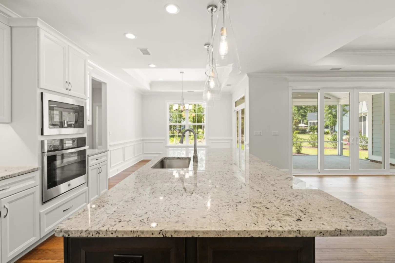 gallery-kitchen (39) Bright kitchen with granite island, pendant lights, and large windows showcasing garden. Ideal setting for a home builder's modern design.