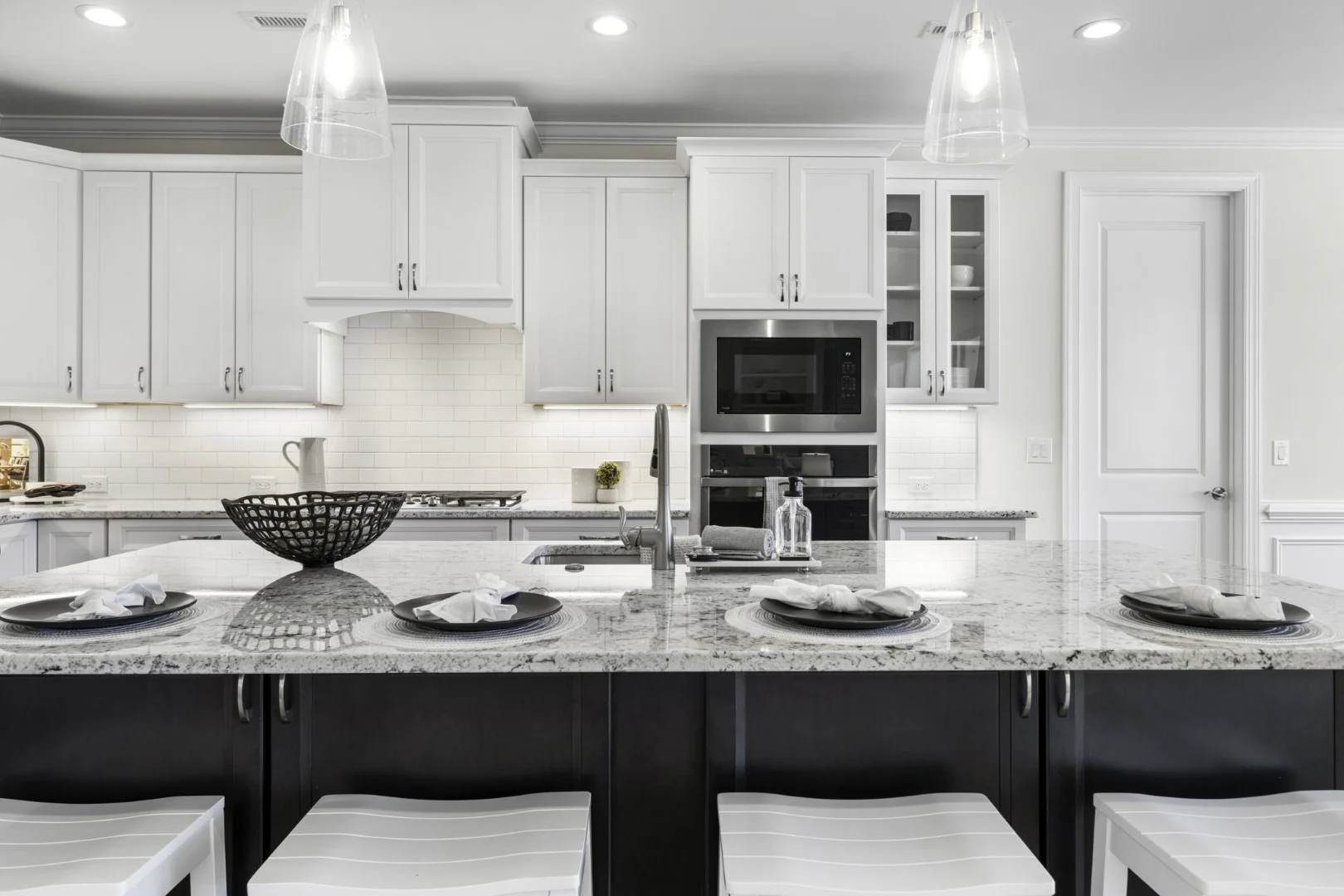 gallery-kitchen (4) Modern kitchen with granite island, white cabinets, black accents, and pendant lights; a home builder's elegant design.