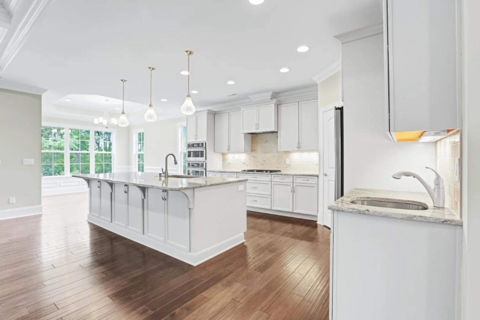 gallery-kitchen (40) Spacious, modern kitchen with white cabinets, large island, pendant lights, and hardwood floors, showcasing home builder expertise.