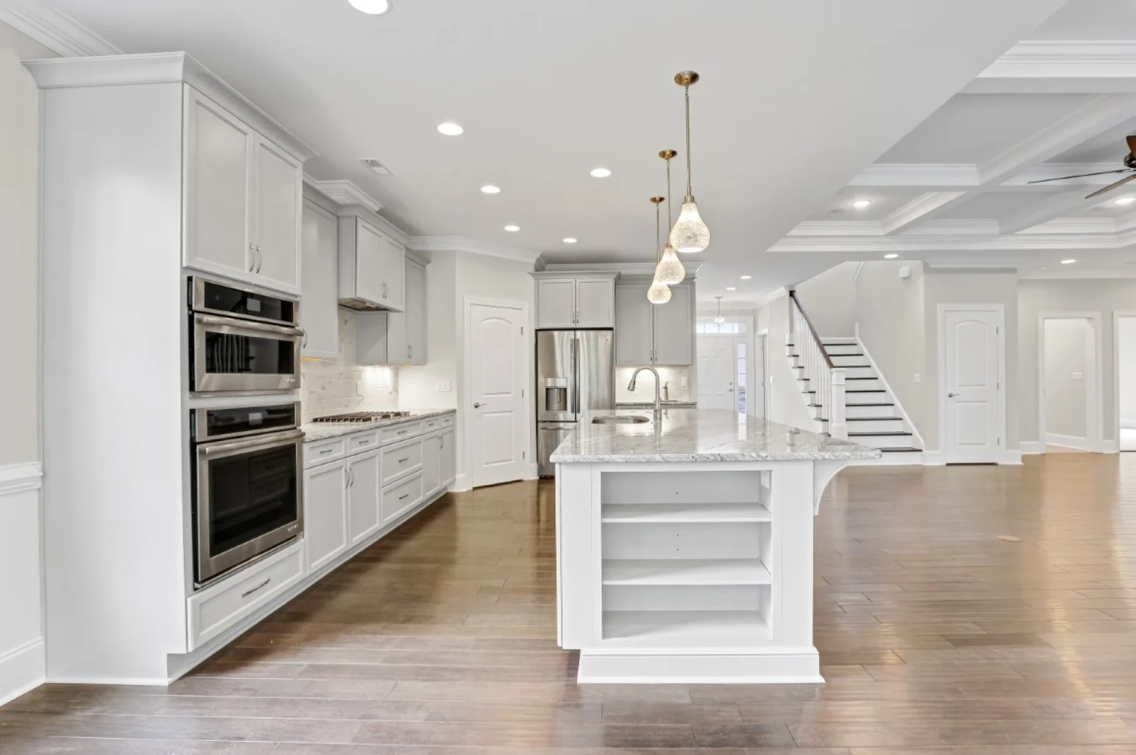 gallery-kitchen (41) Modern kitchen with white cabinetry, granite island, stainless steel appliances, hardwood floor, and staircase designed by a home builder.