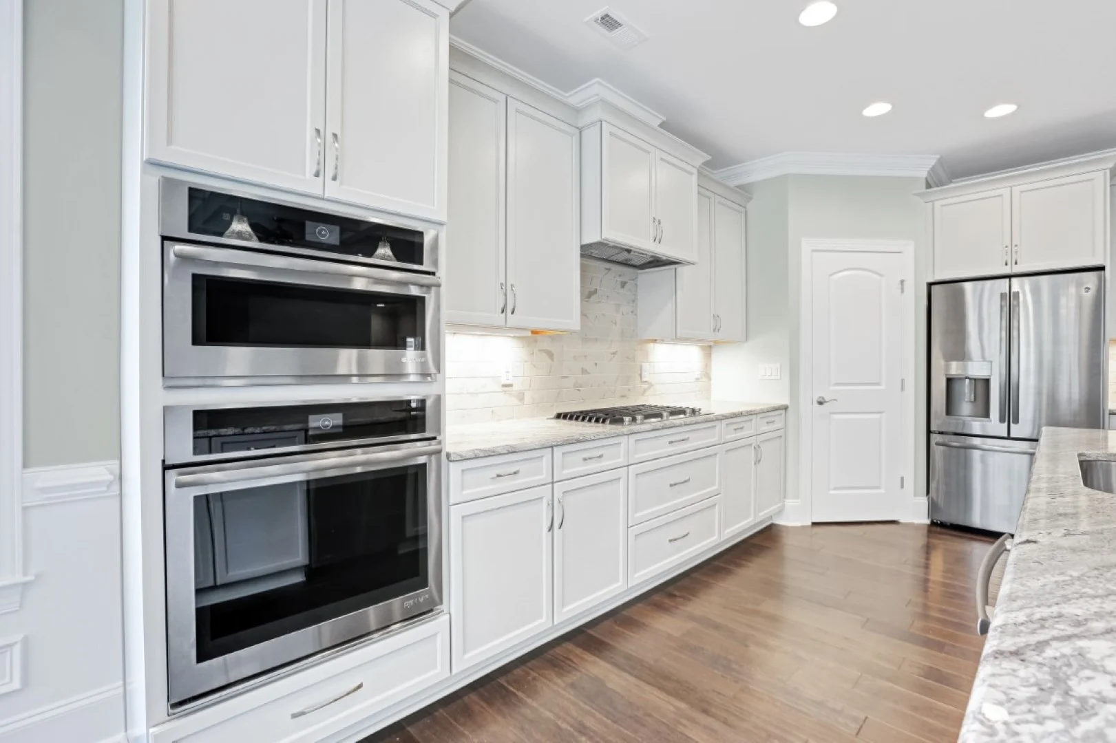 gallery-kitchen (42) Modern kitchen with white cabinets, stainless steel appliances, granite countertops, and hardwood floors, exemplifying home builder craftsmanship.