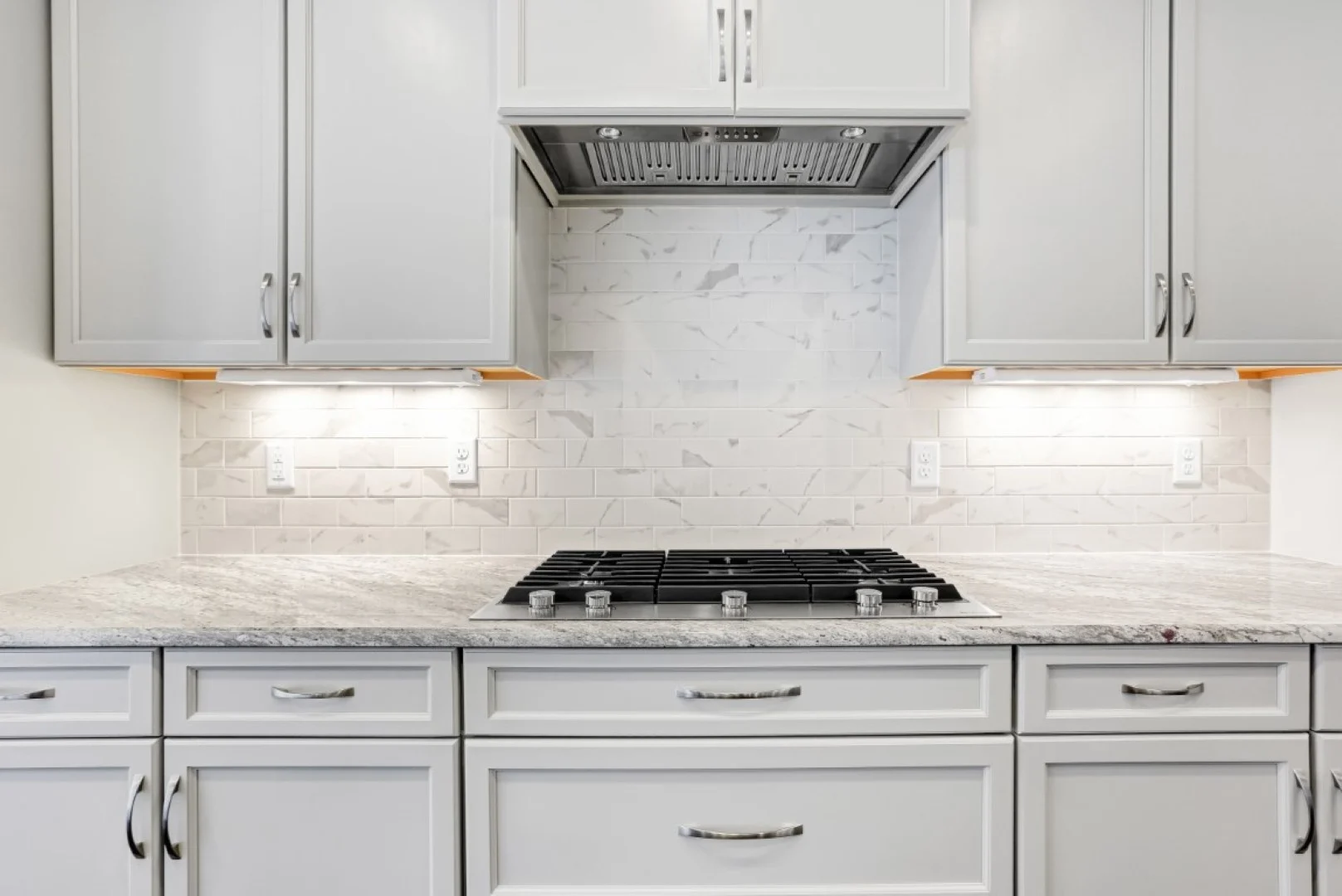 gallery-kitchen (43) Modern kitchen with marble backsplash, white cabinets, and a sleek gas cooktop. Ideal design for home builders seeking elegance and functionality.