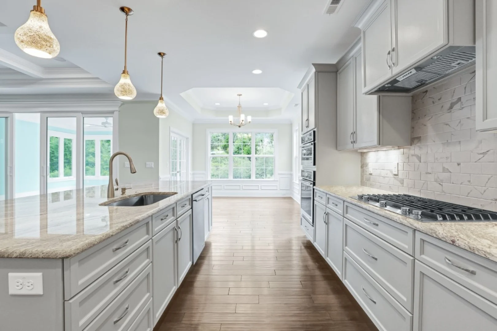 gallery-kitchen (44) Spacious kitchen with island, marble counters, pendant lighting, and large windows. Ideal for a modern home builder design.