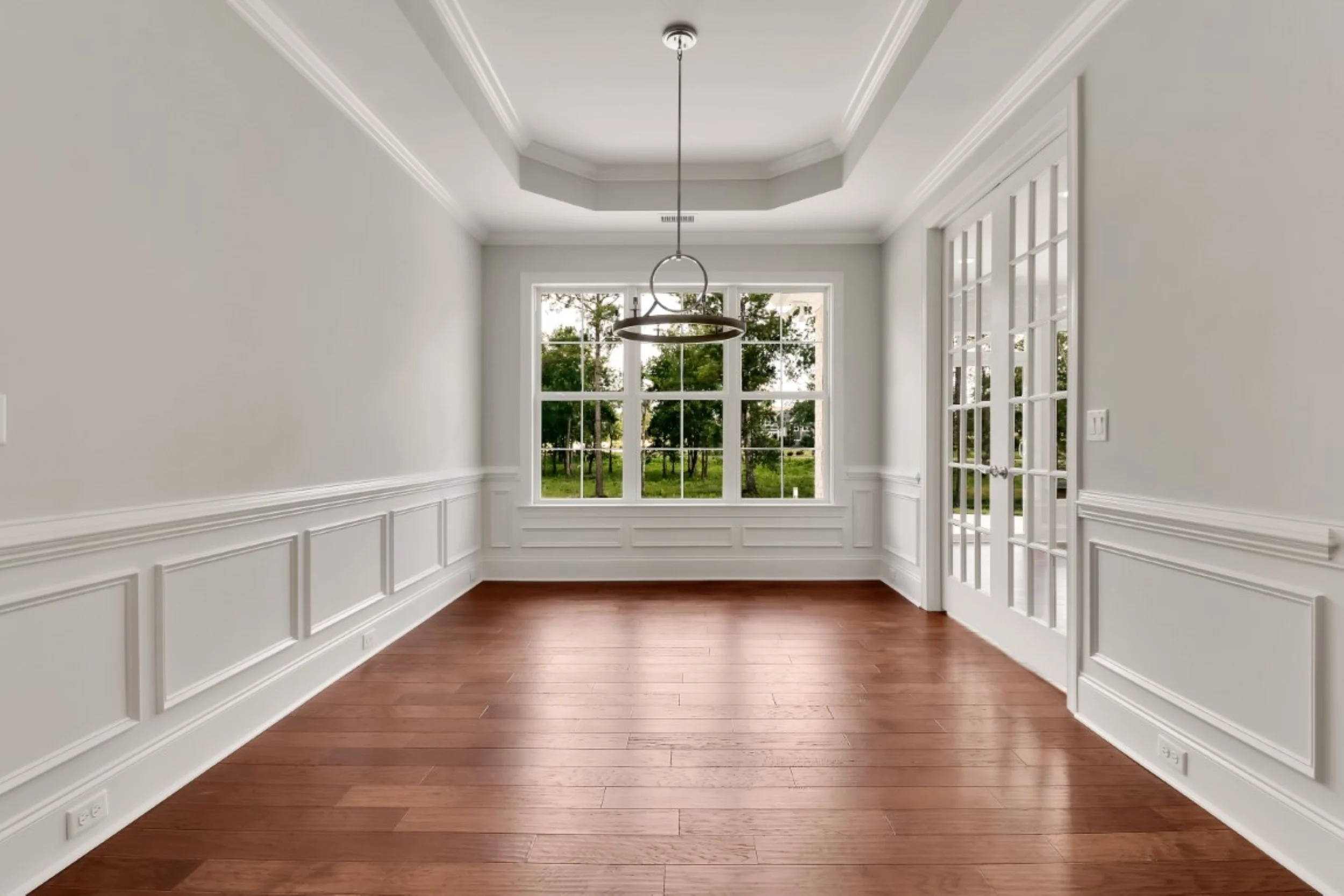 gallery-kitchen (45) Elegant dining room with hardwood floor, tray ceiling, large windows, and glass doors, showcasing the craftsmanship of a home builder.