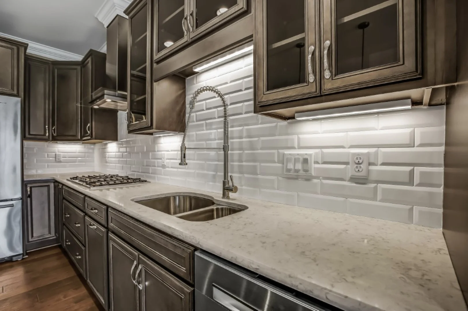 gallery-kitchen (48) Modern kitchen with dark cabinets, stainless steel appliances, white tiled backsplash, and under-cabinet lighting, showcasing home builder expertise.
