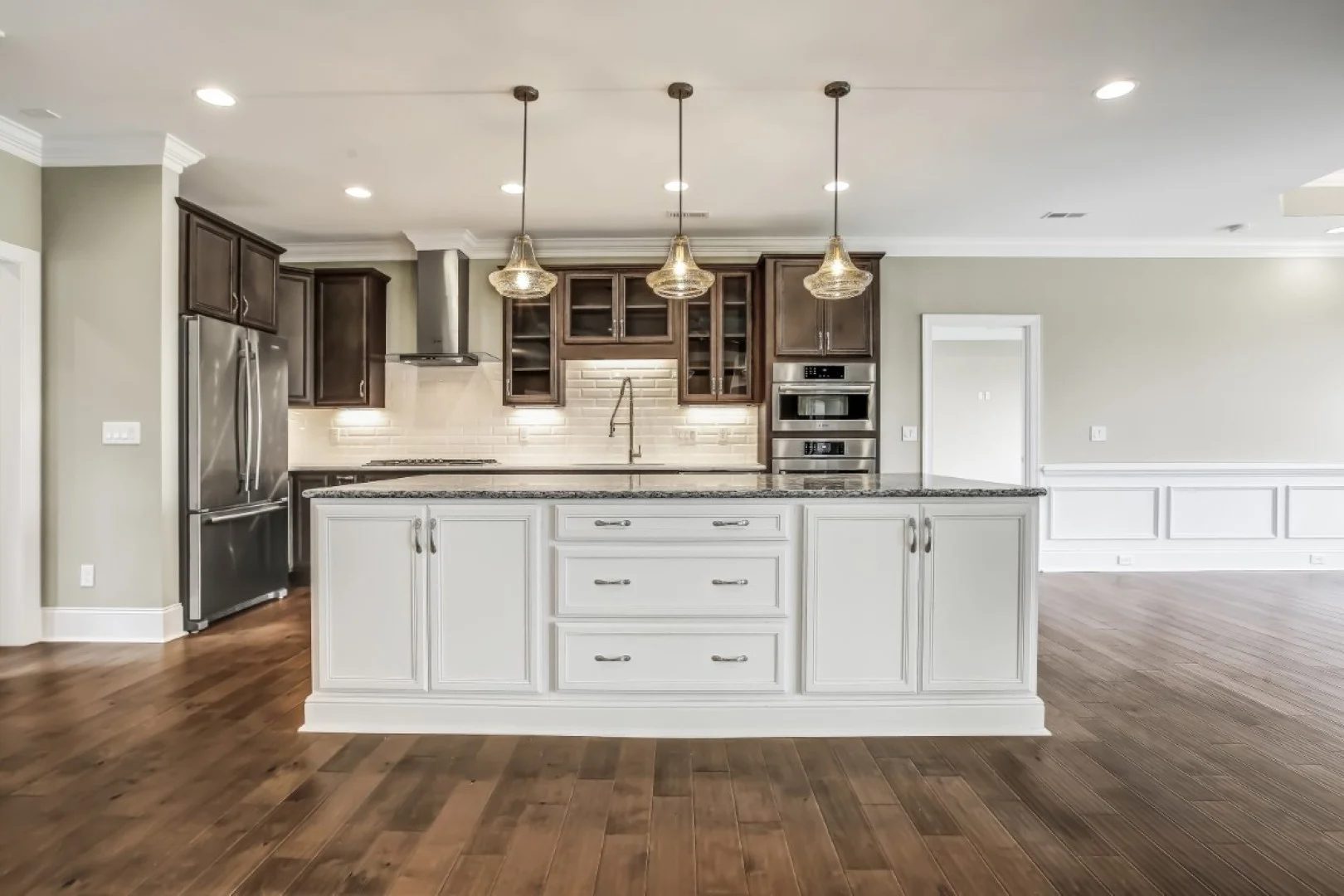gallery-kitchen (49) Modern kitchen designed by a home builder featuring an island, dark wood cabinets, stainless appliances, and pendant lighting over hardwood floors.