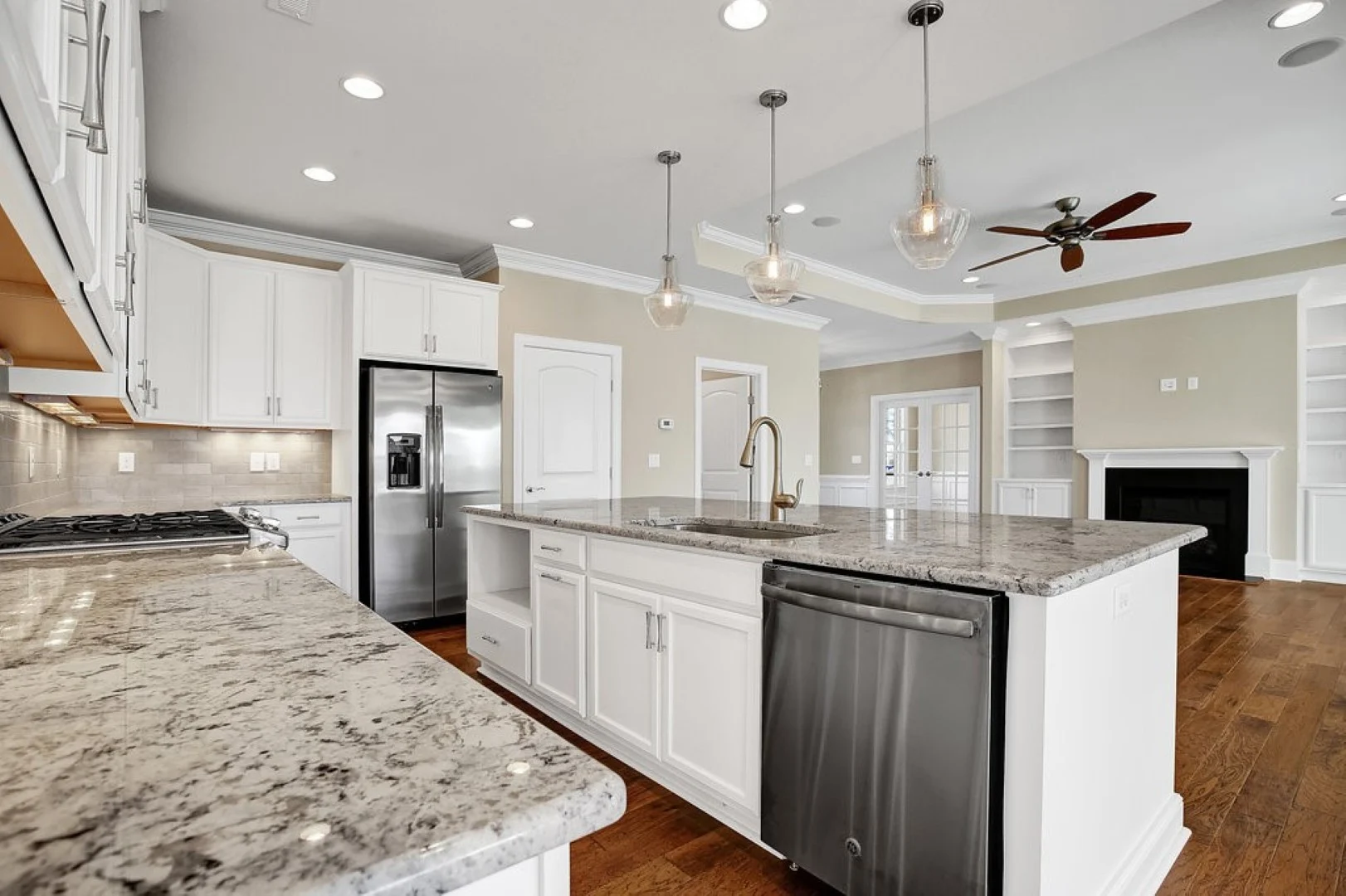 gallery-kitchen (50) Modern kitchen with granite countertops, white cabinets, stainless steel appliances, pendant lights, and hardwood flooring, designed by a home builder