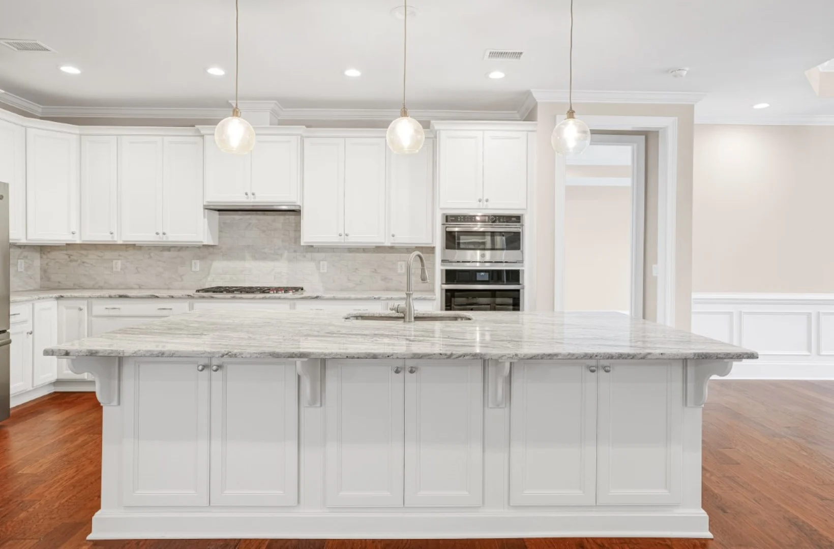 gallery-kitchen (51) Modern kitchen with white cabinets, large marble island, and pendant lights; ideal showcase for a home builder's craftsmanship.