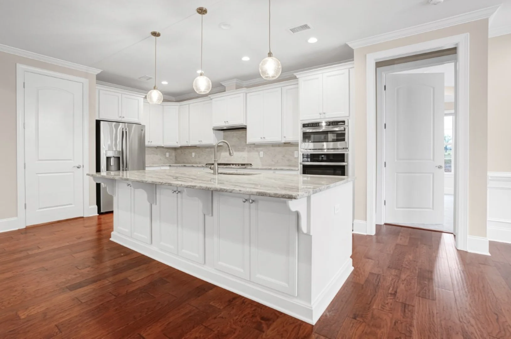 gallery-kitchen (52) Modern kitchen with white cabinetry, marble island, pendant lights, stainless steel appliances, and hardwood floors, designed by home builder.