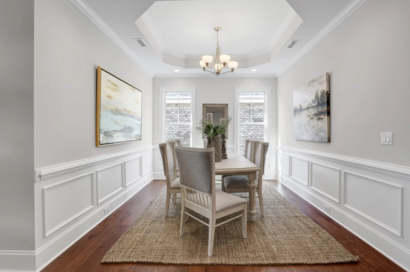 gallery-kitchen (55) Elegant dining room with paneled walls, cozy rug, art, and chandelier by home builder. Light streaming through windows highlights the decor.