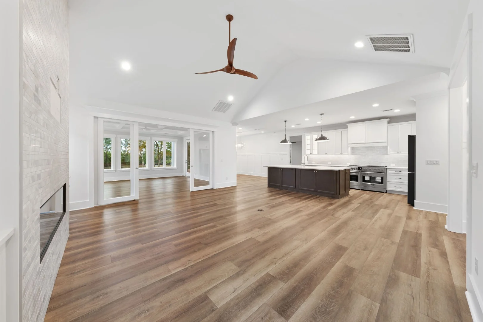 gallery-kitchen (7) Spacious open-concept living and kitchen area with wood flooring, modern island, ceiling fan, large windows, and neutral tones; ideal for a home build