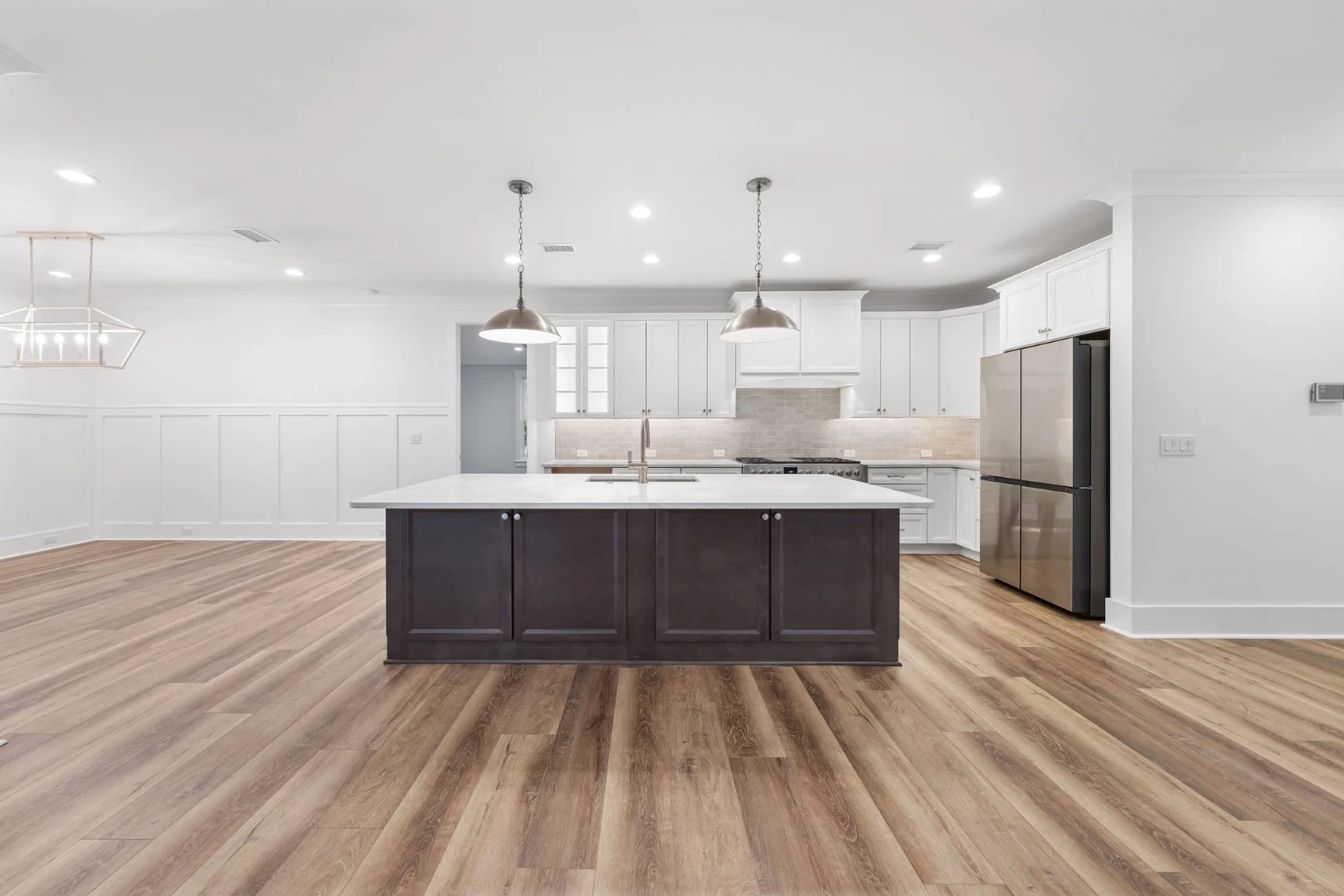 gallery-kitchen (8) Modern kitchen with dark island, white cabinets, stainless steel appliances, wood floors, and pendant lights, showcasing home builder design.