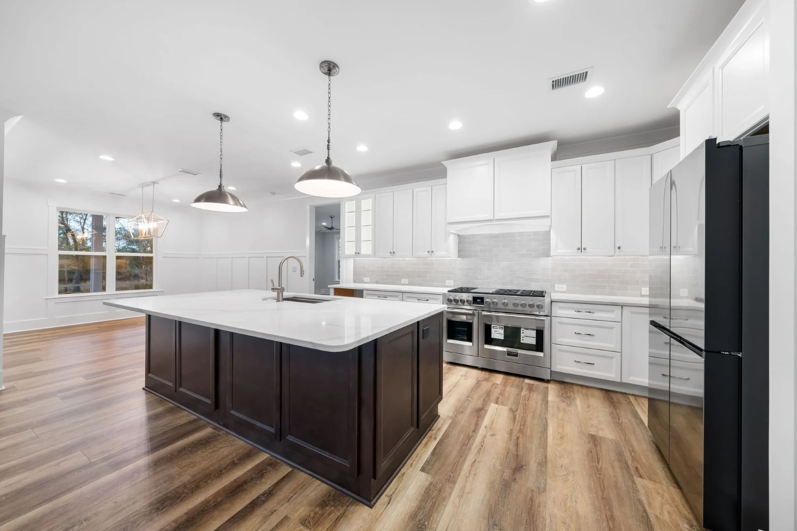 gallery-kitchen (9) Modern kitchen with white cabinetry, large island, wood floors, and stainless appliances. Pendant lights enhance the space, showcasing home builder de
