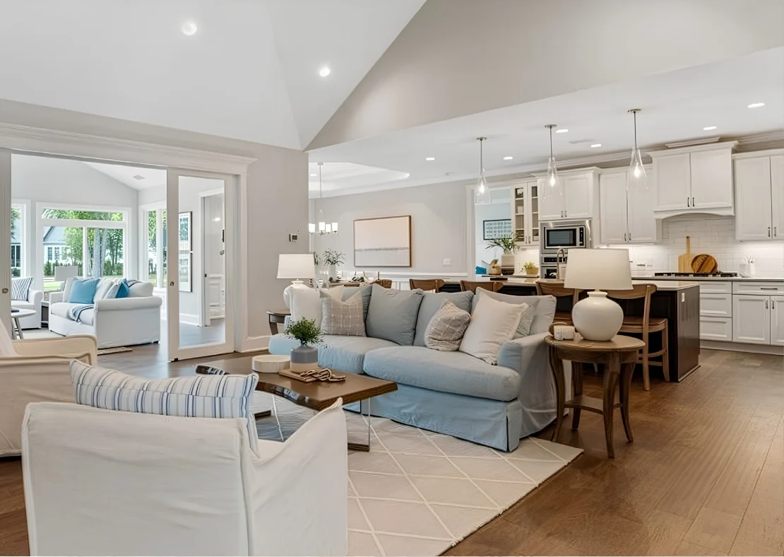 Modern open-concept living area and kitchen with soft blue and white decor, large windows, and hardwood floors, highlighting a skilled home builder's 