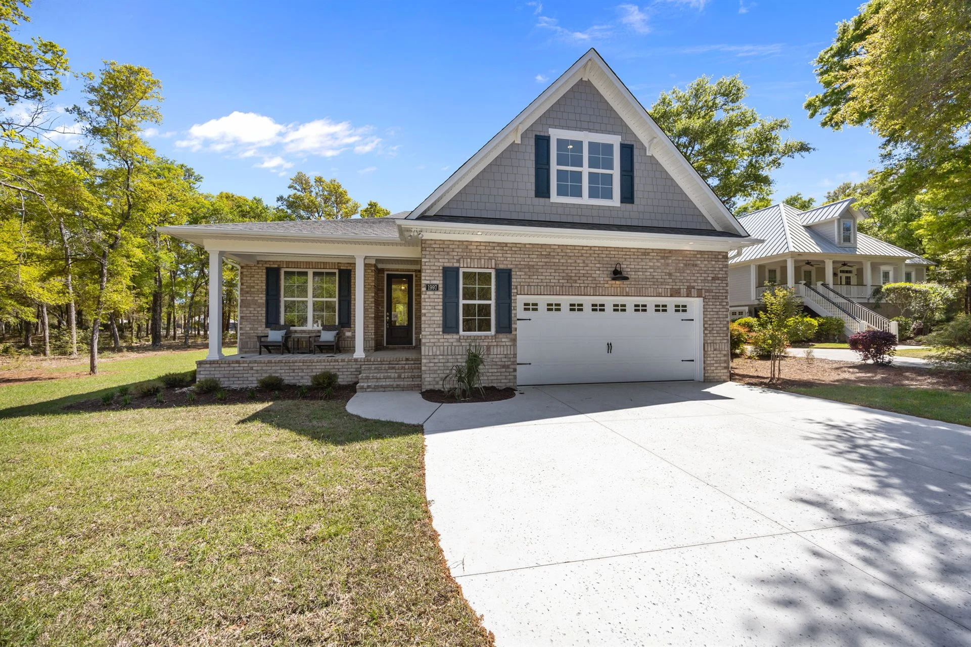 Brick home with attached garage, porch, and large driveway, surrounded by trees under a blue sky, created by a home builder.