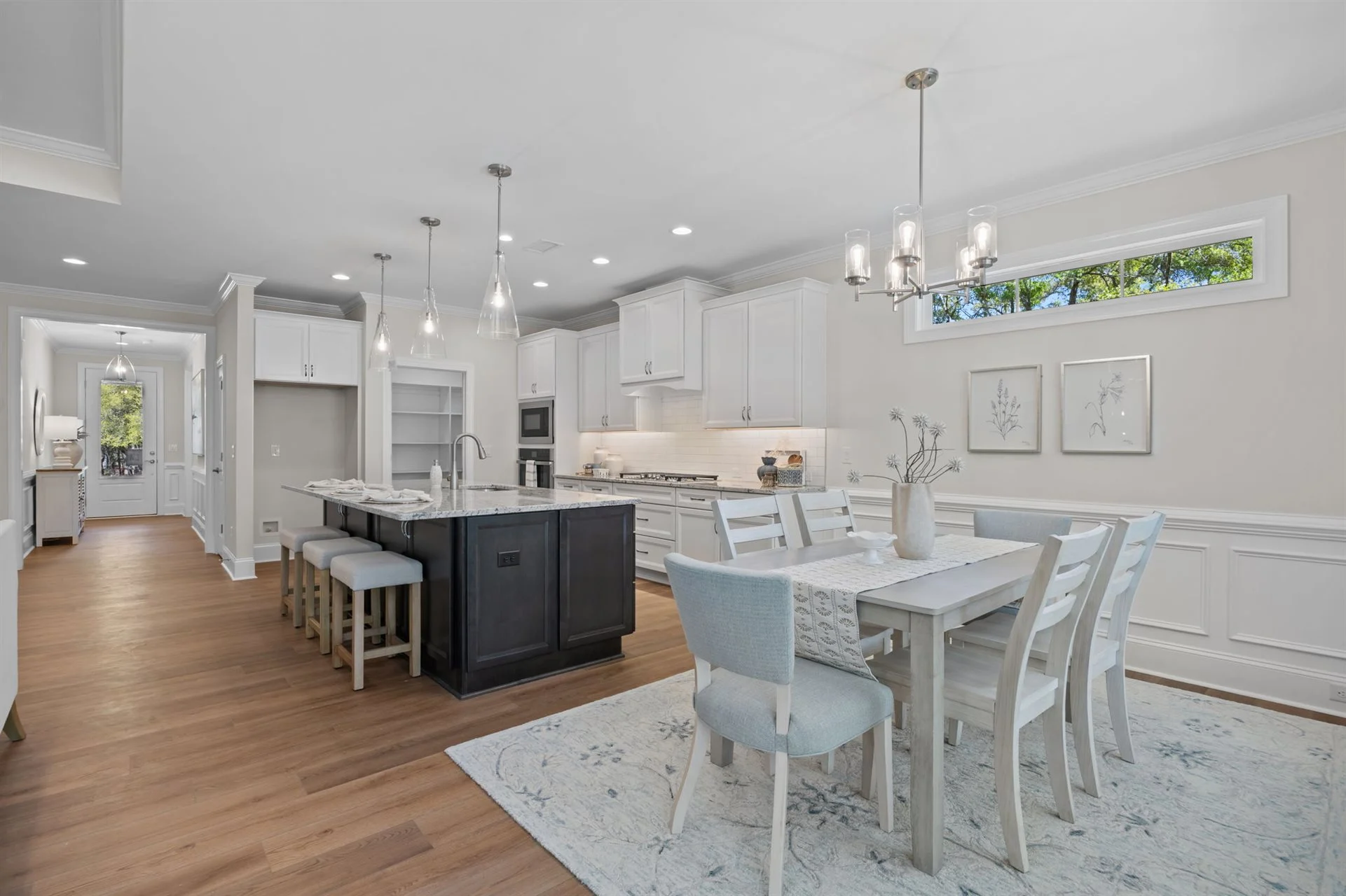 Modern kitchen and dining area with white cabinetry, black island, elegant lighting, and light wood flooring, showcasing home builder design.