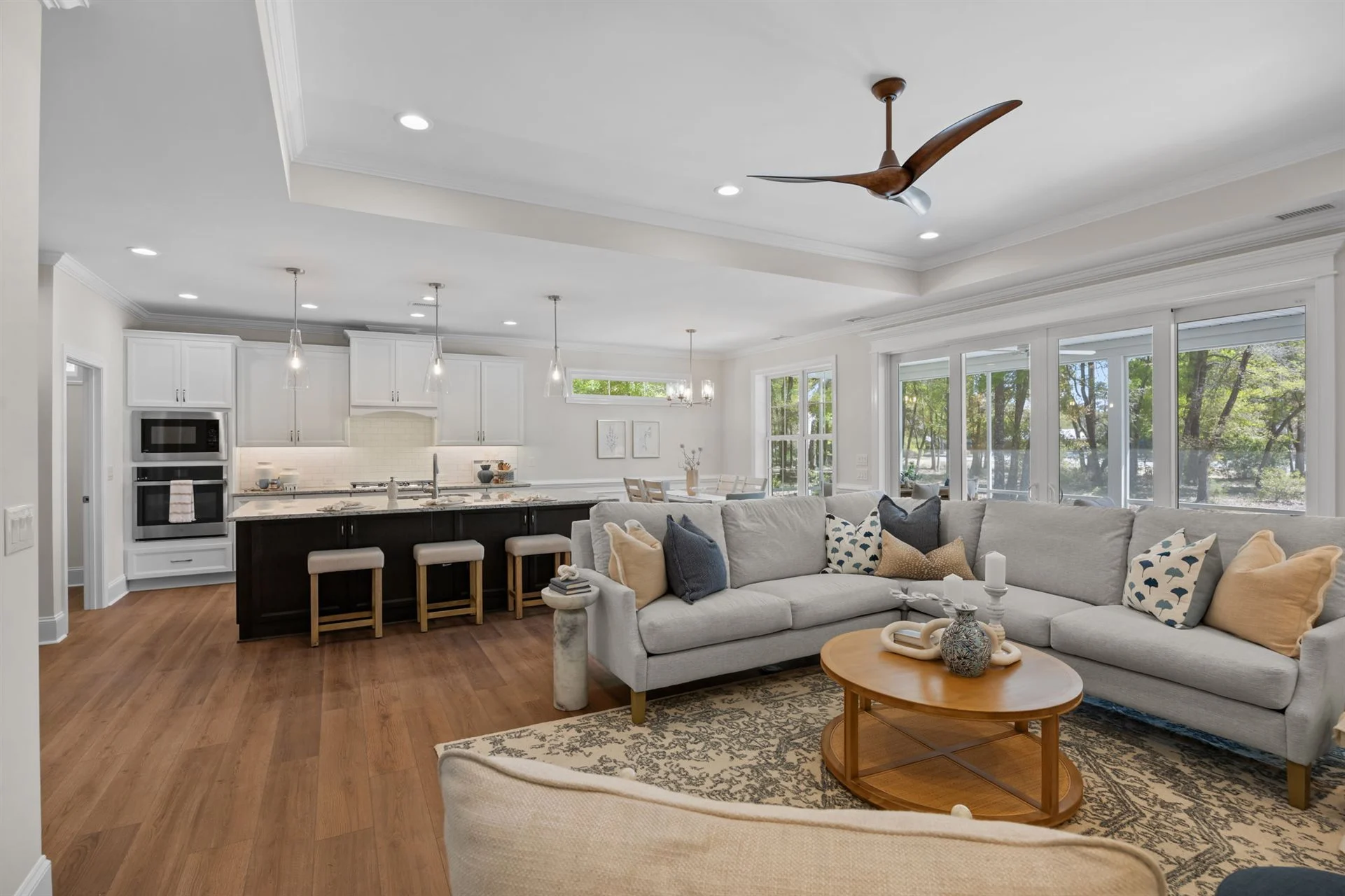 Spacious open-concept living area with large sofa, modern kitchen, wooden flooring, and ample natural light, ideal for a home builder's design.