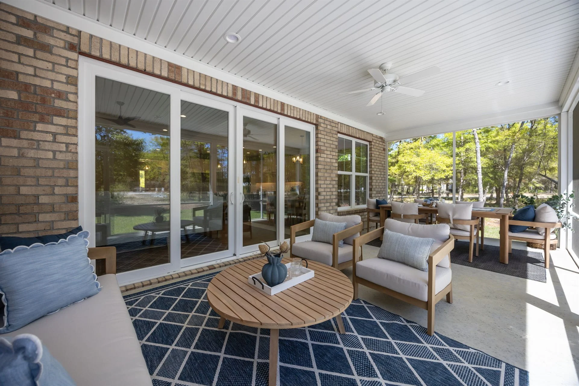 Spacious sunroom with modern seating, wood accents, and blue decor. Glass doors open to a lush backyard, showcasing home builder craftsmanship.